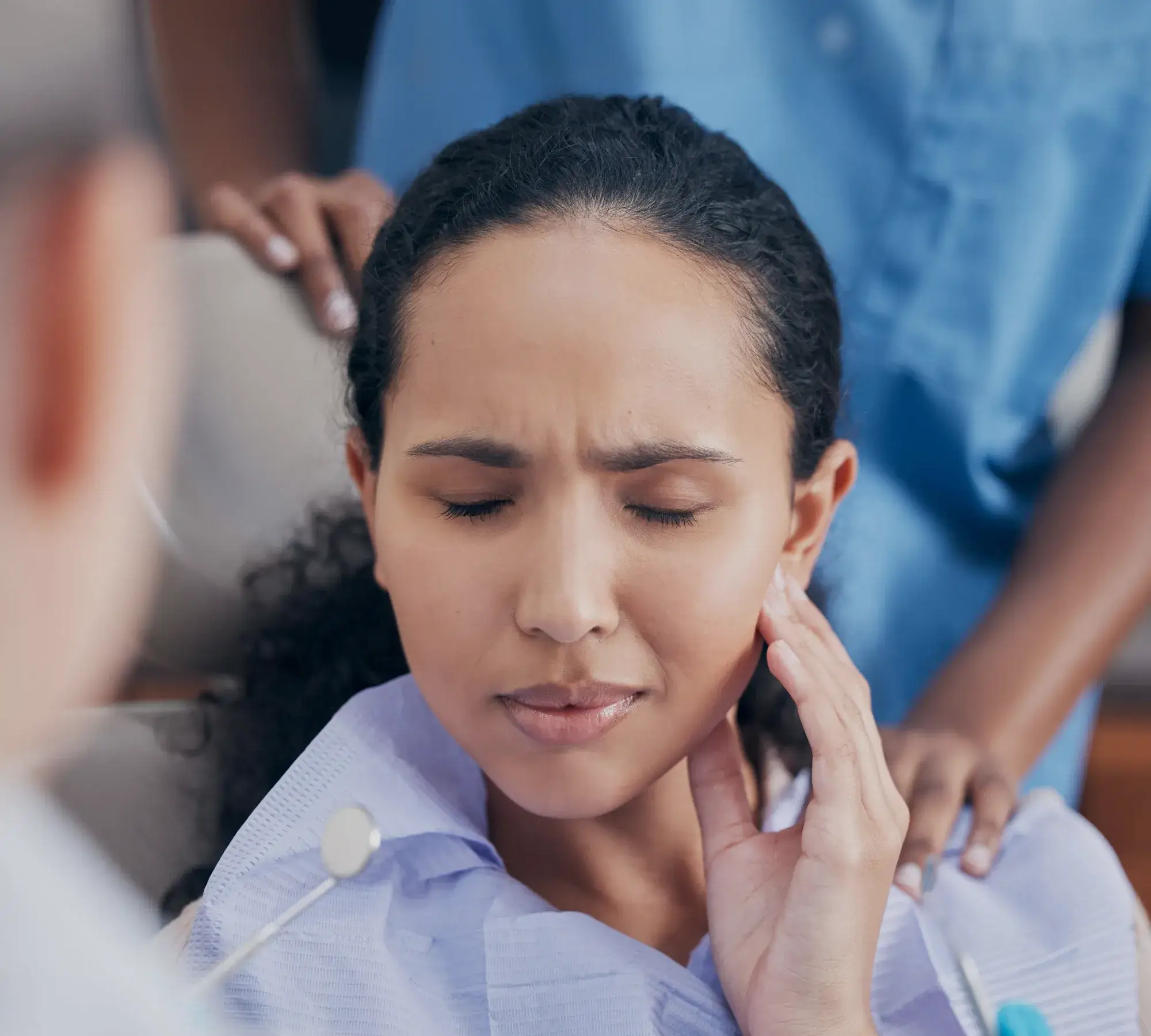 Woman in dental bib with eyes closed holding her jaw in pain during dental exam.
