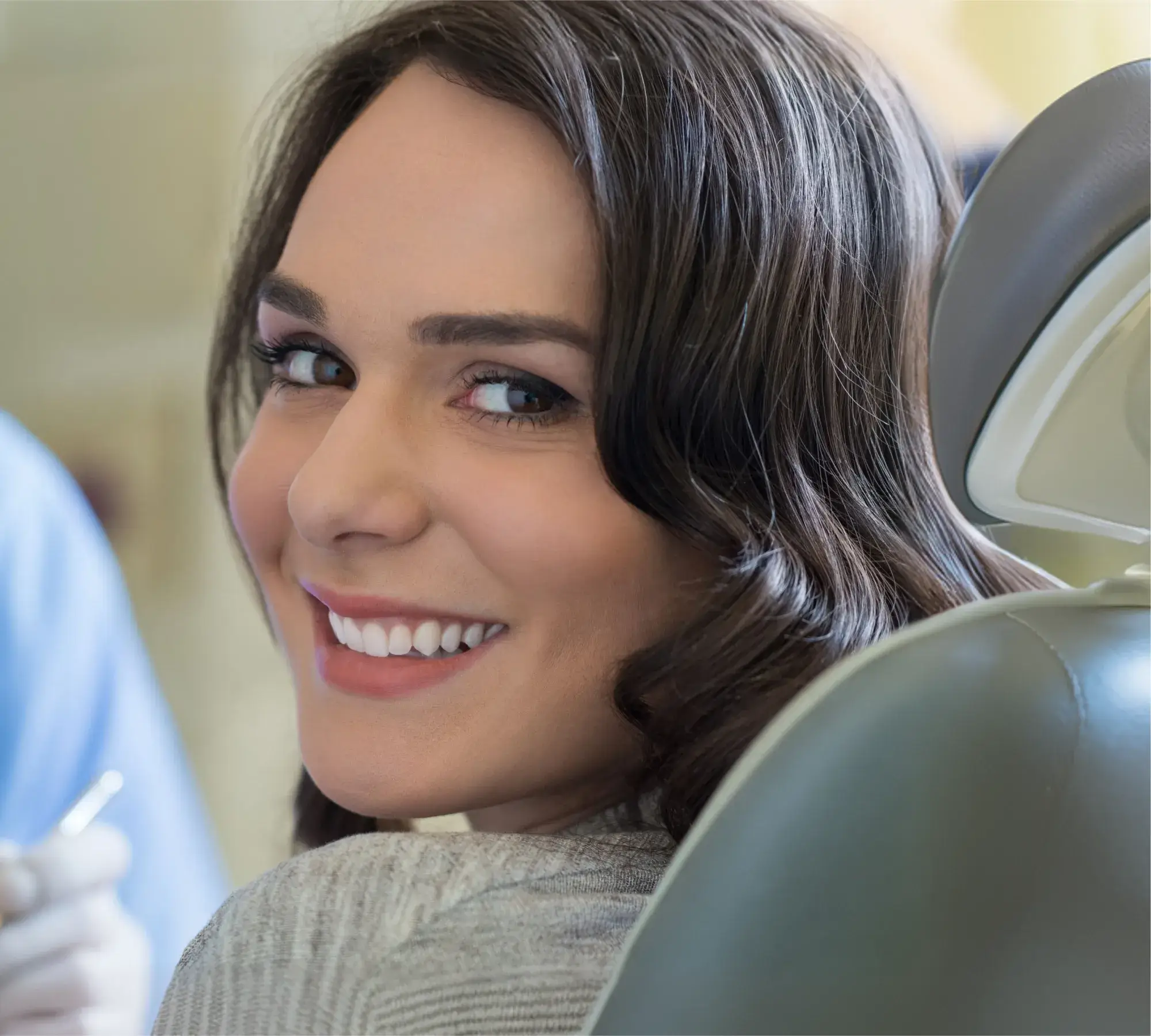 Smiling woman with dark hair sitting in a dental chair looking back over her shoulder.