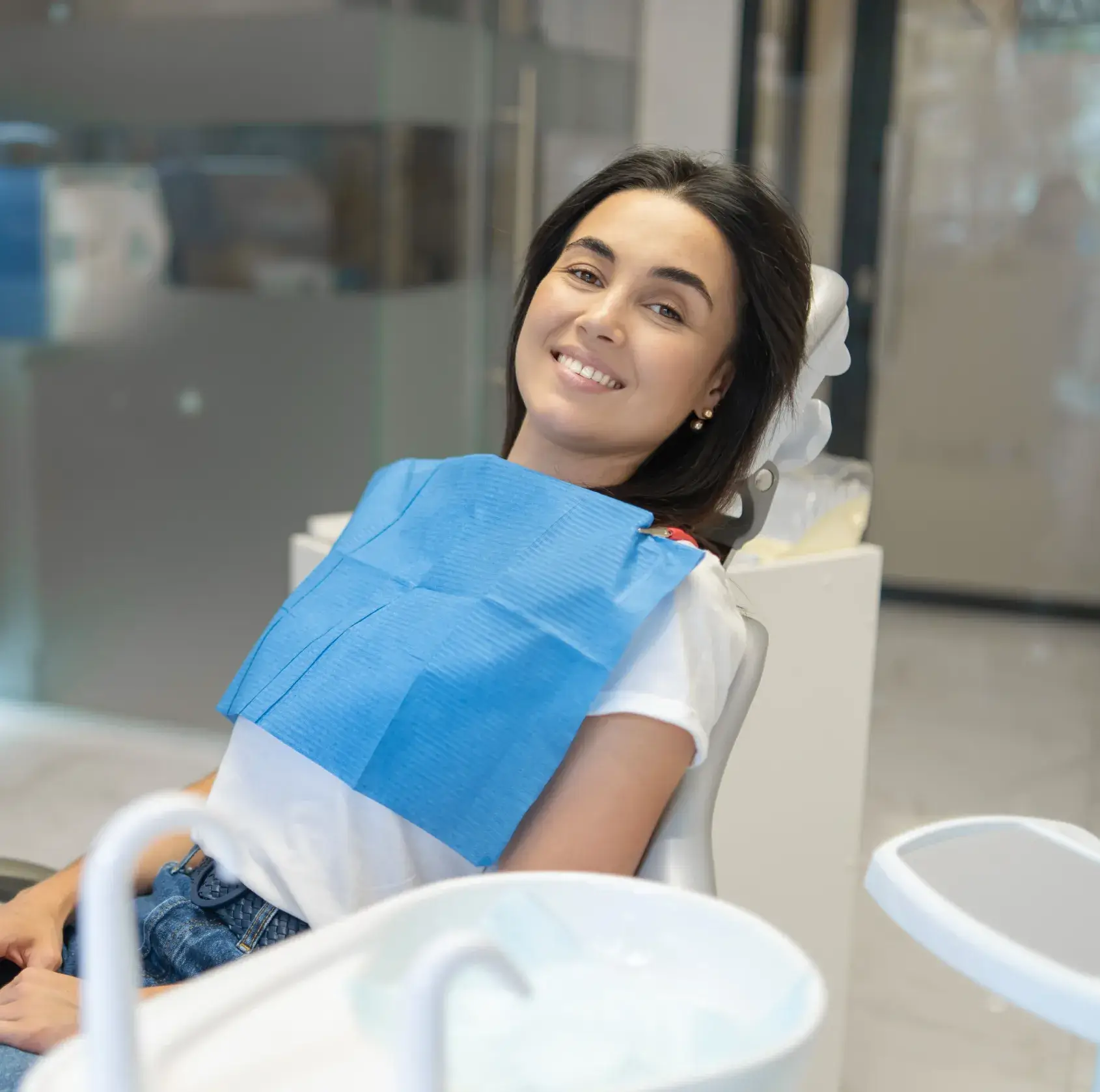 Smiling woman in dental chair wearing a blue bib in a bright dental office.