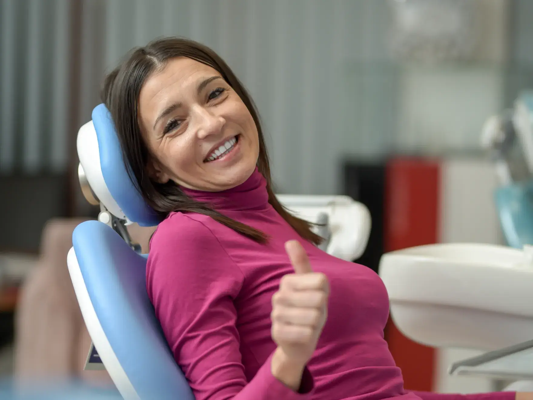 Smiling woman in a dental chair showing thumbs up, indicating a positive dental experience.