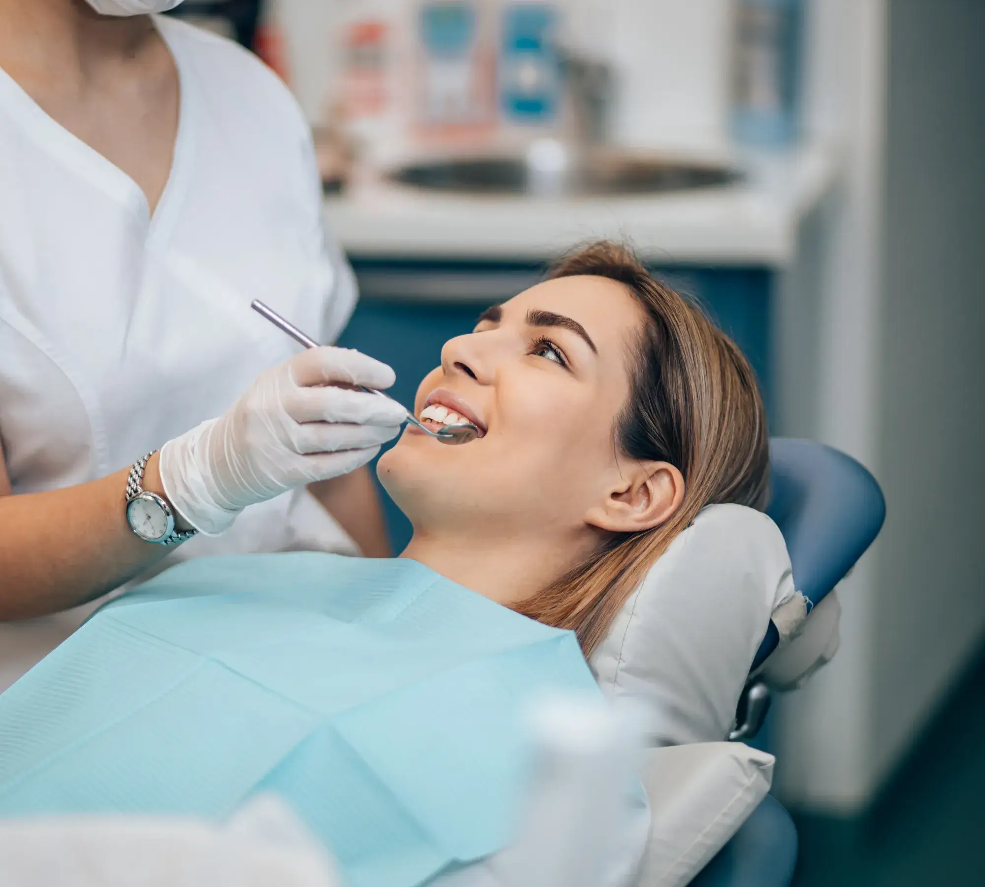 Woman smiling while a dentist wearing gloves examines her teeth with a dental mirror.