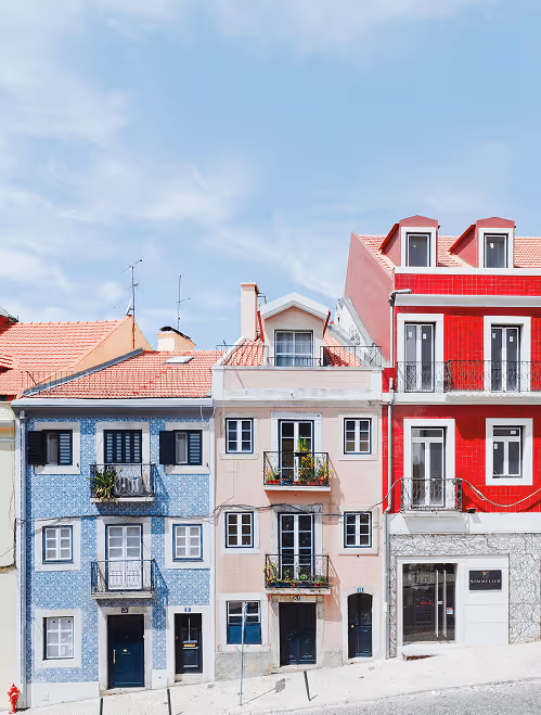 Row of colorful multi-story houses with balconies under a bright blue sky.