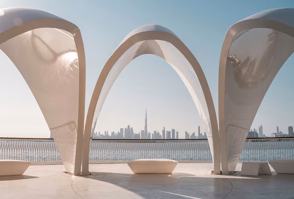 Modern white curved architectural arches framing a distant city skyline across the water on a clear day.