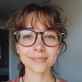 Close-up of a smiling person wearing round glasses with a blurred background.
