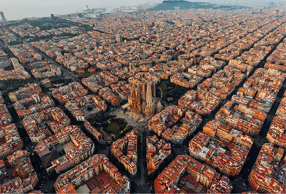 Aerial view of Barcelona showing the Sagrada Família church surrounded by grid-pattern city blocks.