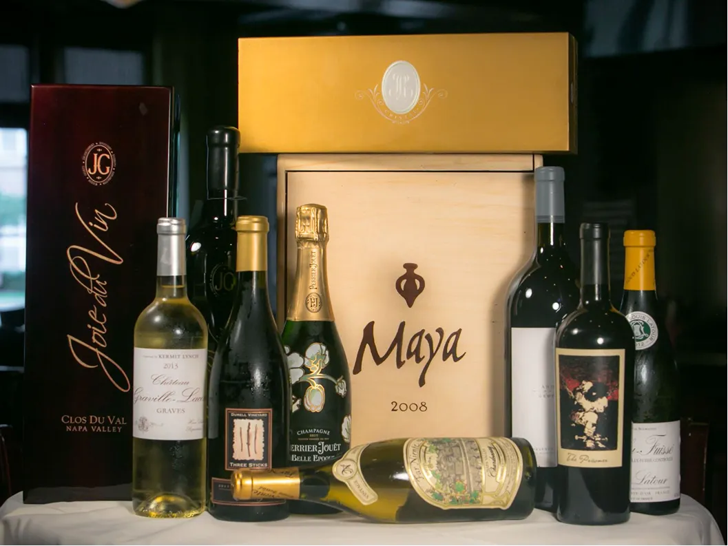 Variety of wine bottles displayed in front of wooden and cardboard wine boxes.
