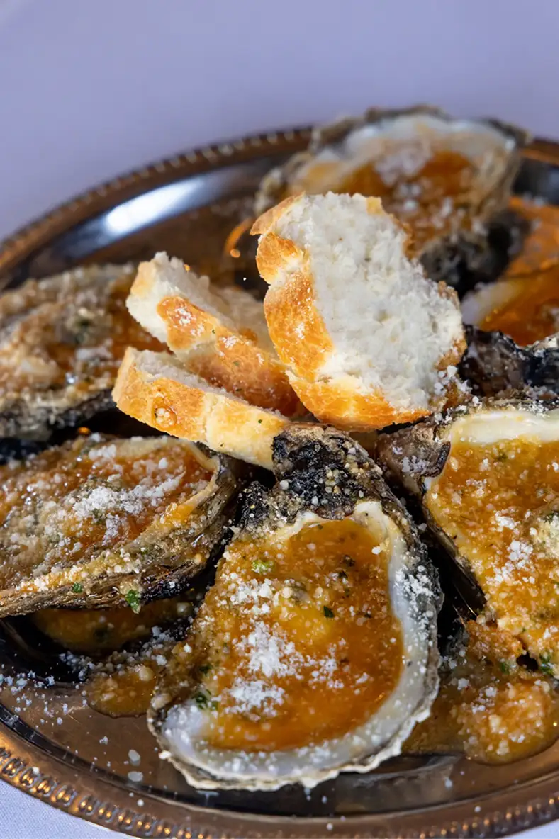 Plate of baked oysters topped with cheese and breadcrumbs, served with slices of crusty bread.