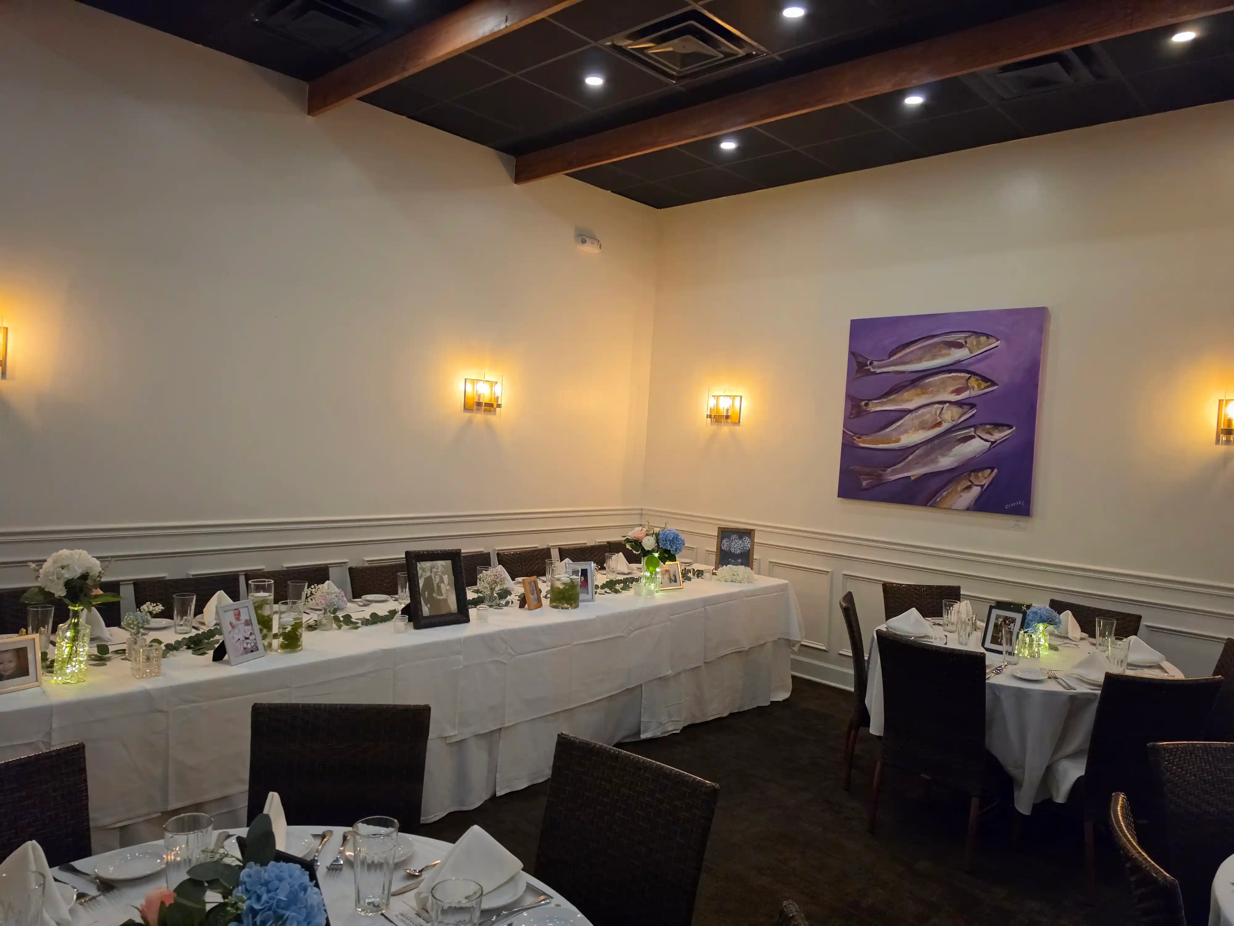 Cozy dining room with tables set in white and brown linens and a painting of fish on purple background.