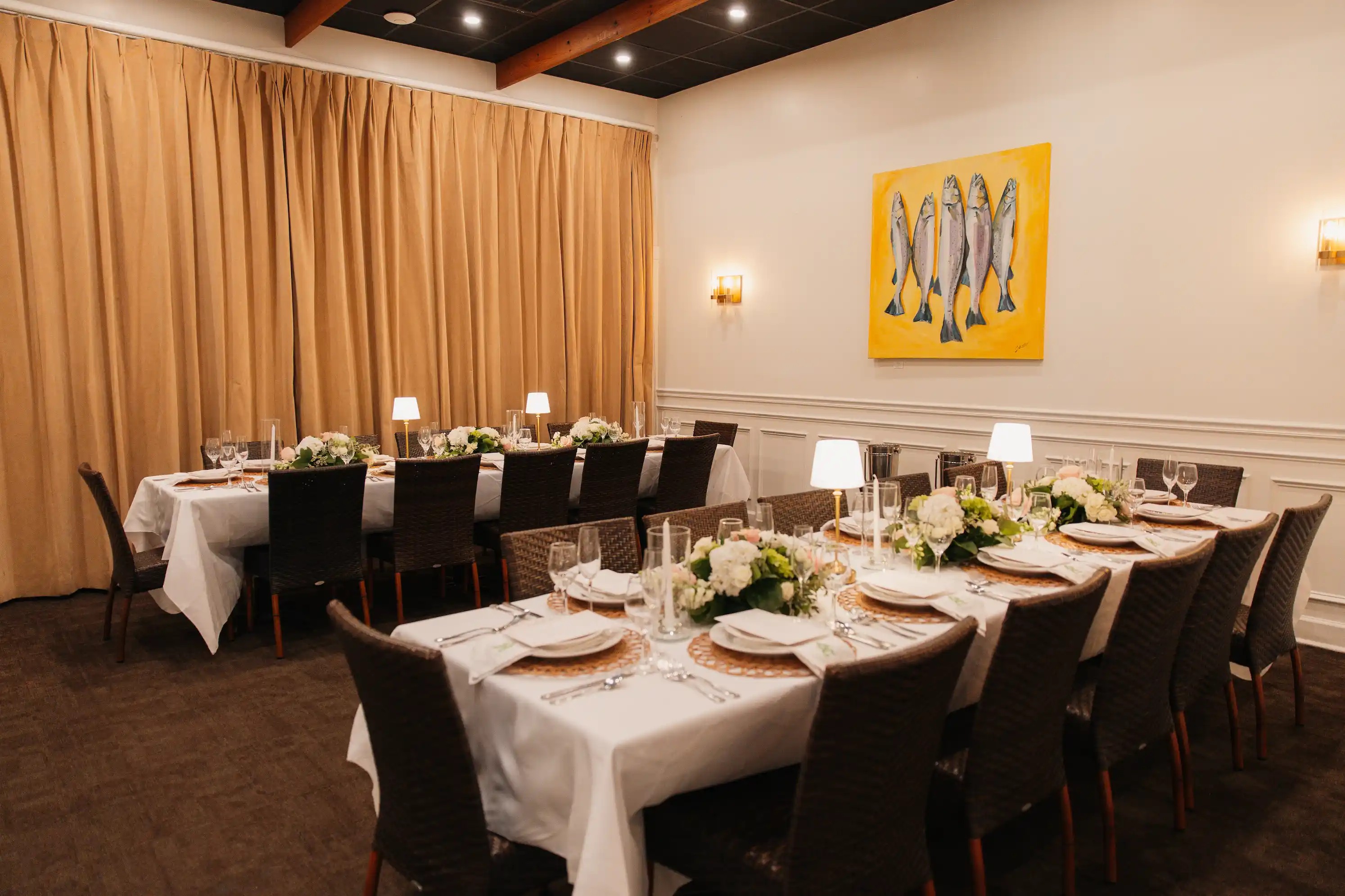 Empty dining room with tables set with glasses, white napkins, and a fish painting on the wall.