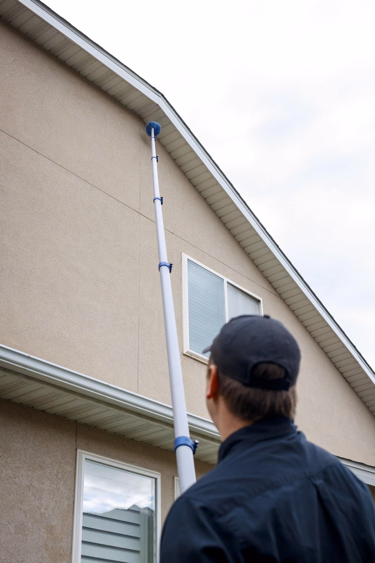 Technician using an extension pole to treat the roofline of a Utah home for pests