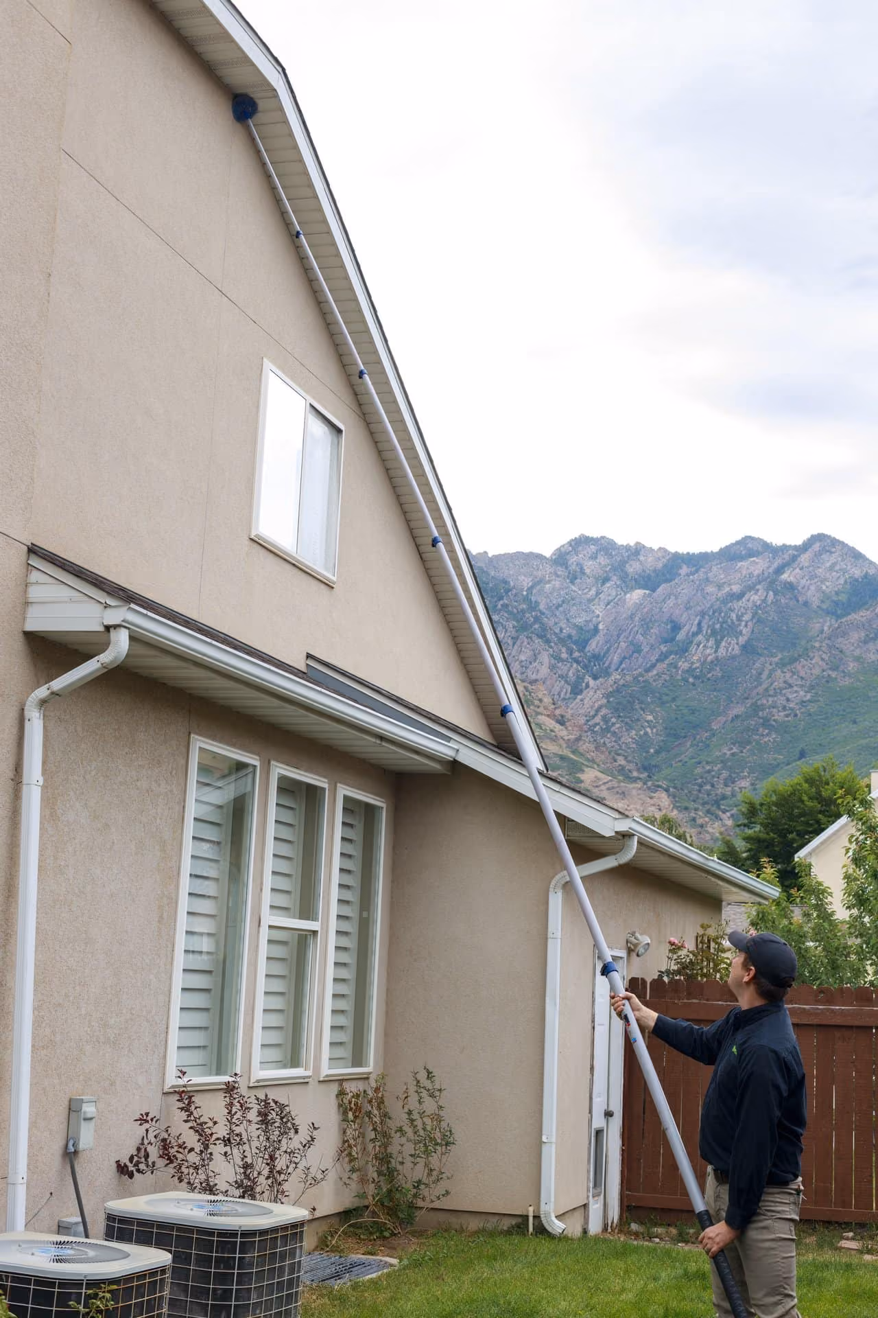 Technician removing spider webs from the eaves of a Utah home with an extension pole