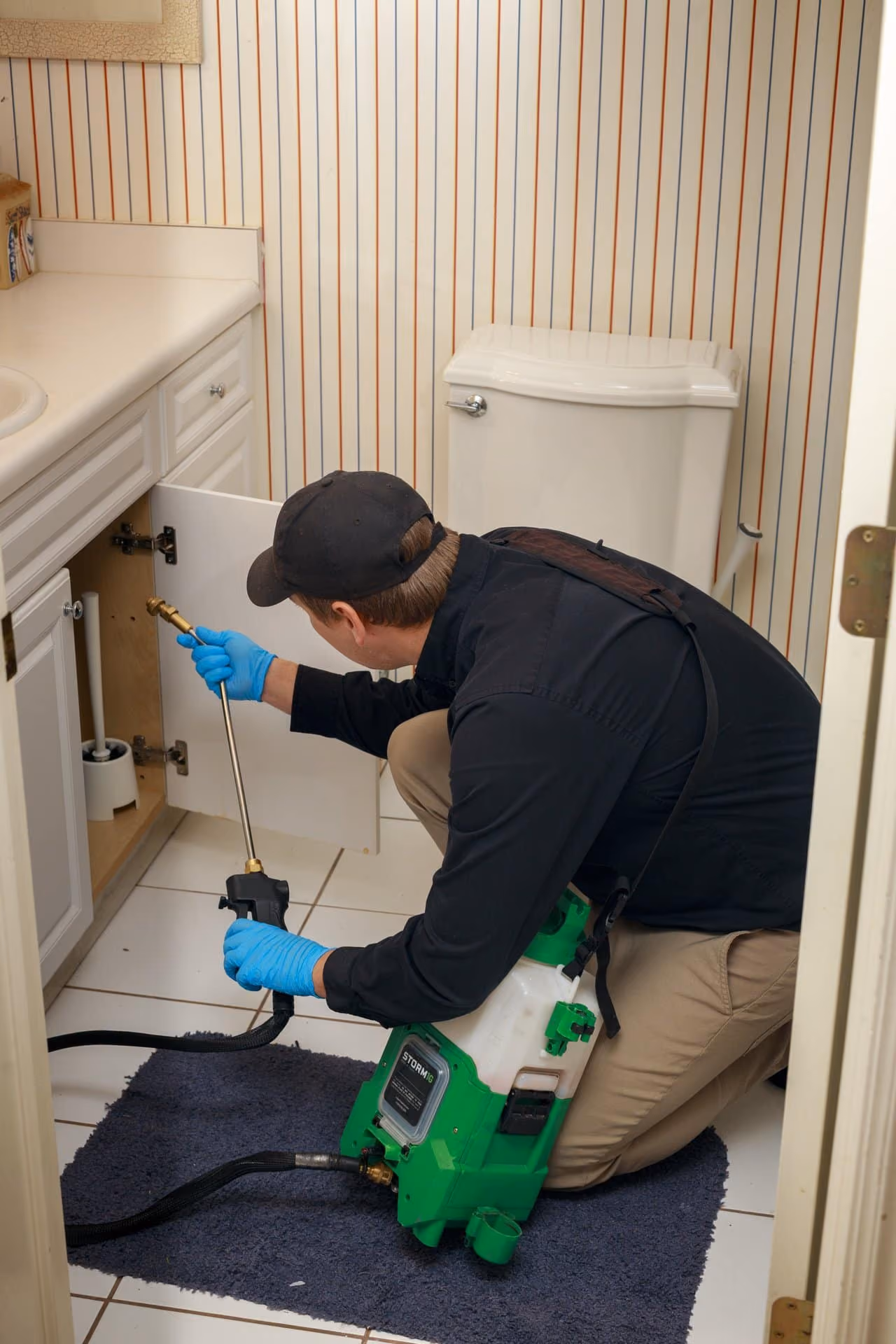 Technician treating under a bathroom sink during an indoor pest control visit in Utah