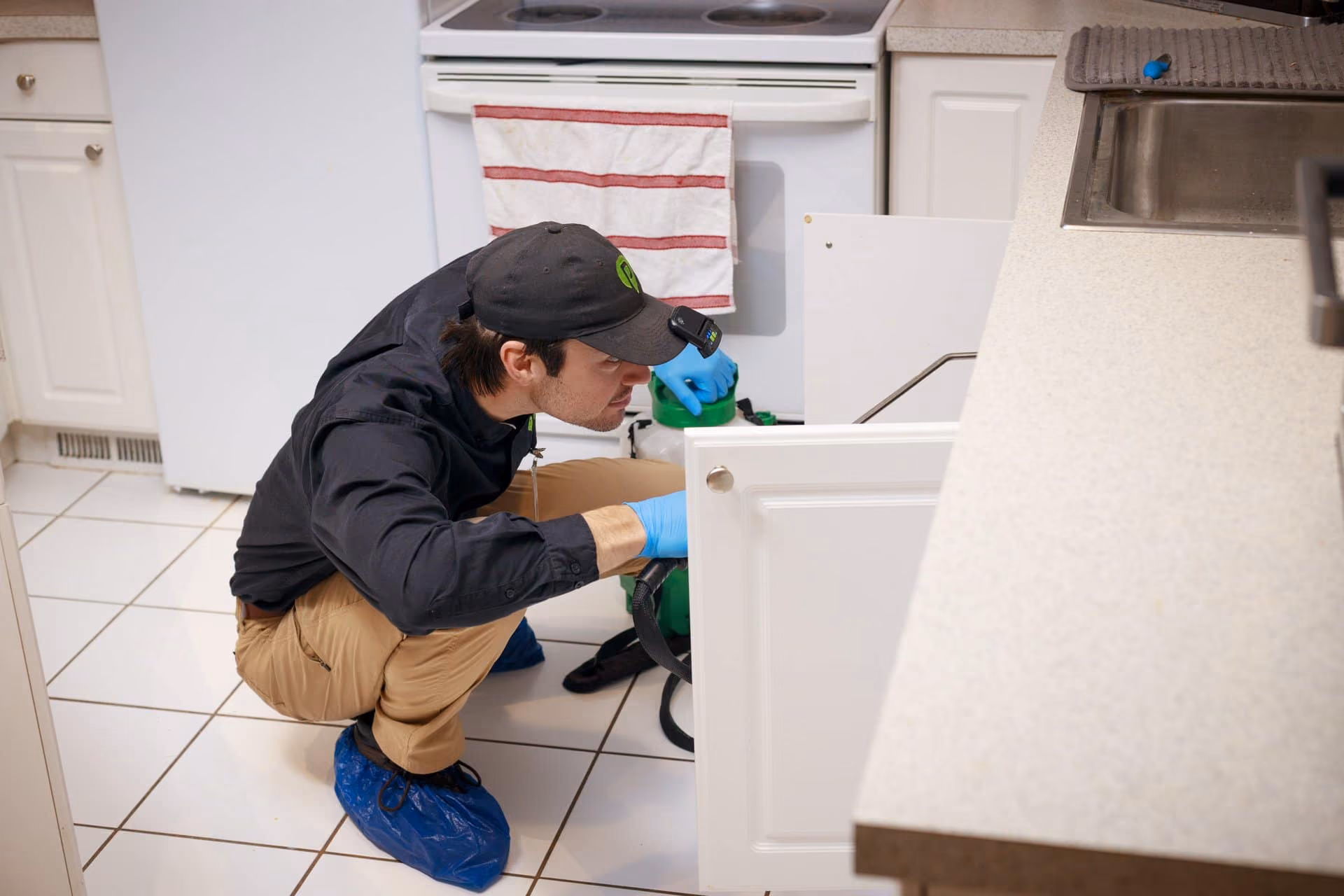 Pest Pro technician inspecting behind a kitchen appliance during an indoor pest inspection
