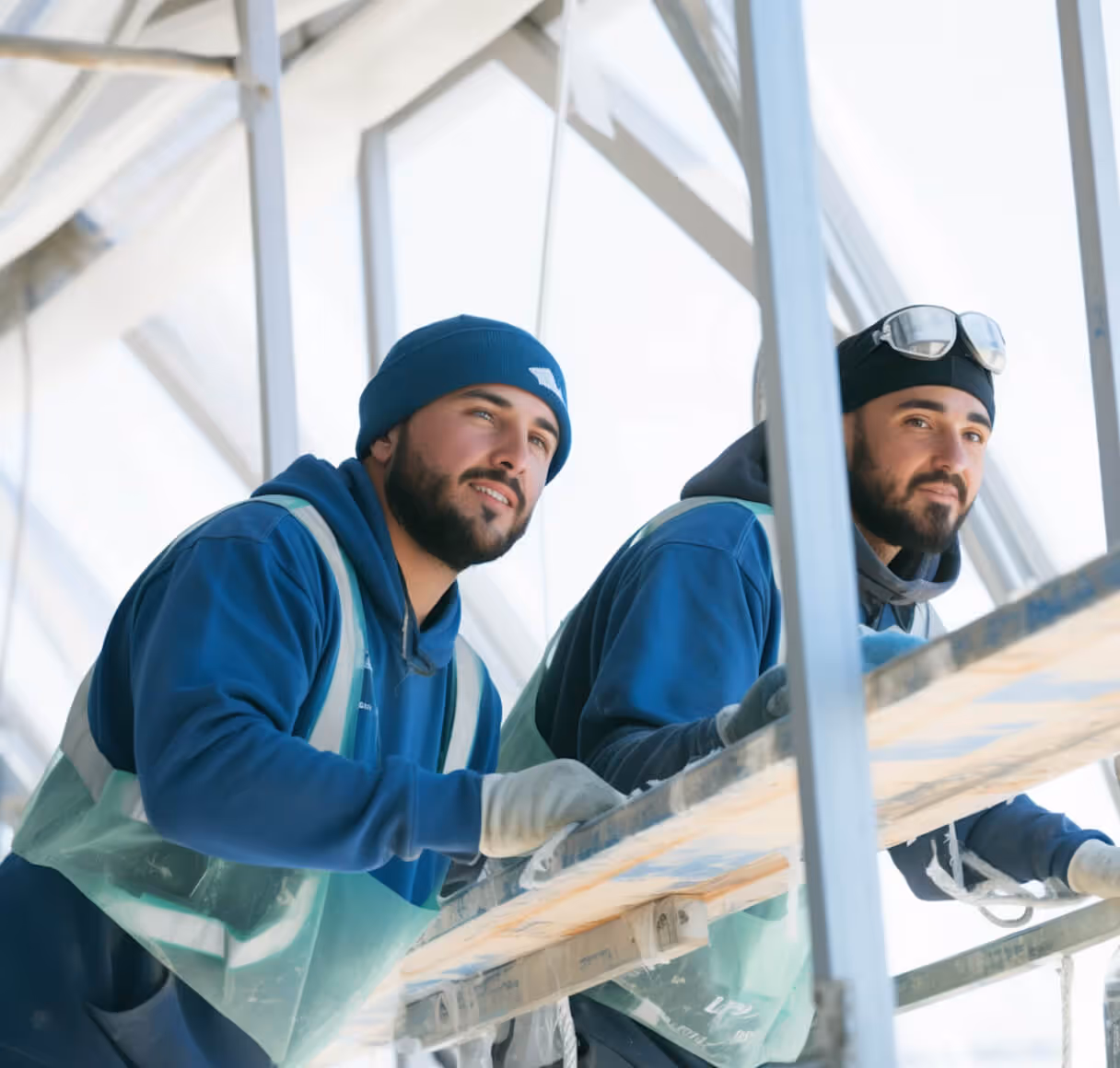 Two men collaborating on a construction site, wearing hard hats and safety vests, surrounded by building materials.