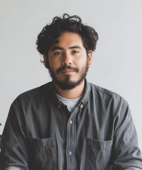 A man with curly hair and a beard is seated at a desk, focused on his work.
