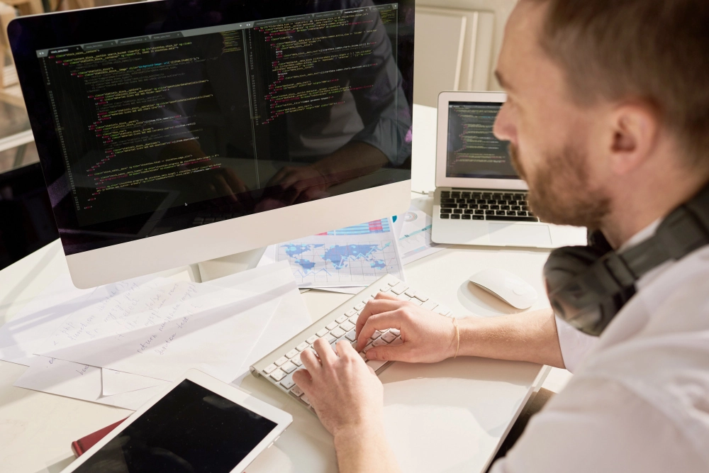 Two men working together at a desk on a computer with code displayed on the screen.