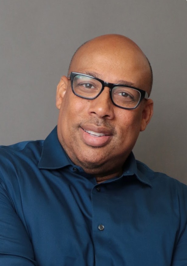 Ainsley C. Rudolfo professional headshot smiling in blue shirt