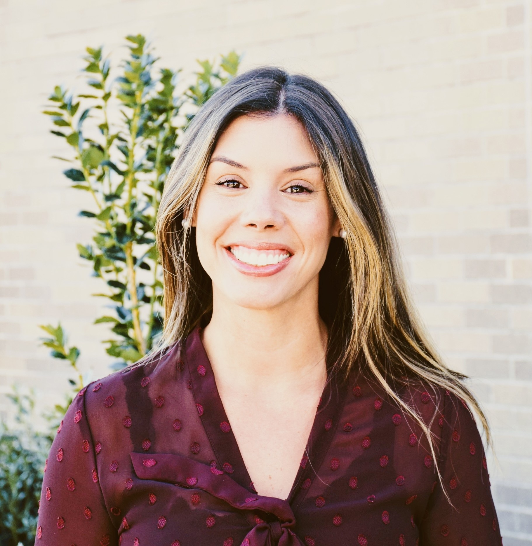Kristin Donnelly smiling outdoors near brick wall and shrubs