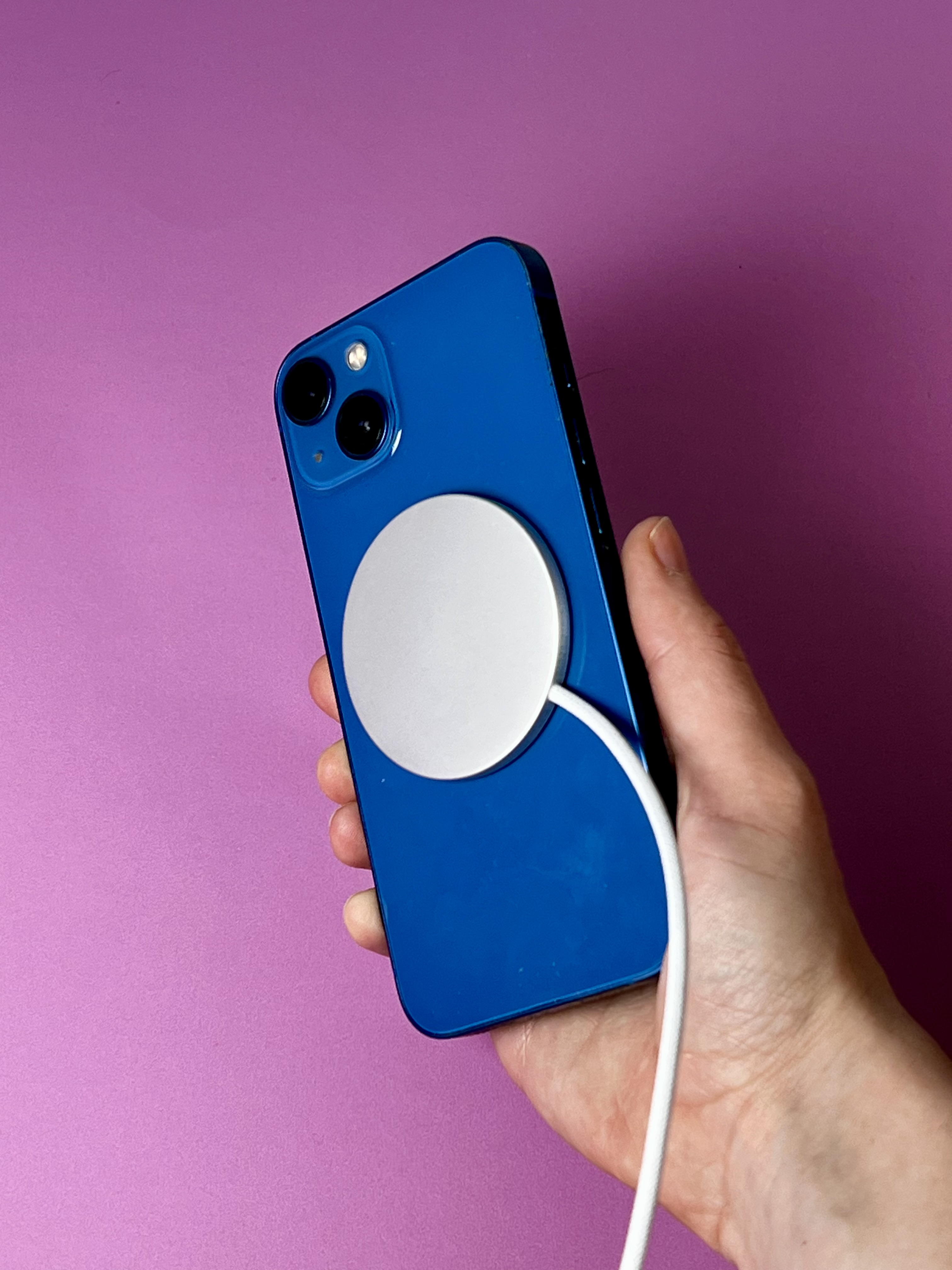 A flat circular charger is attached magnetically to the back of a blue iPhone.
