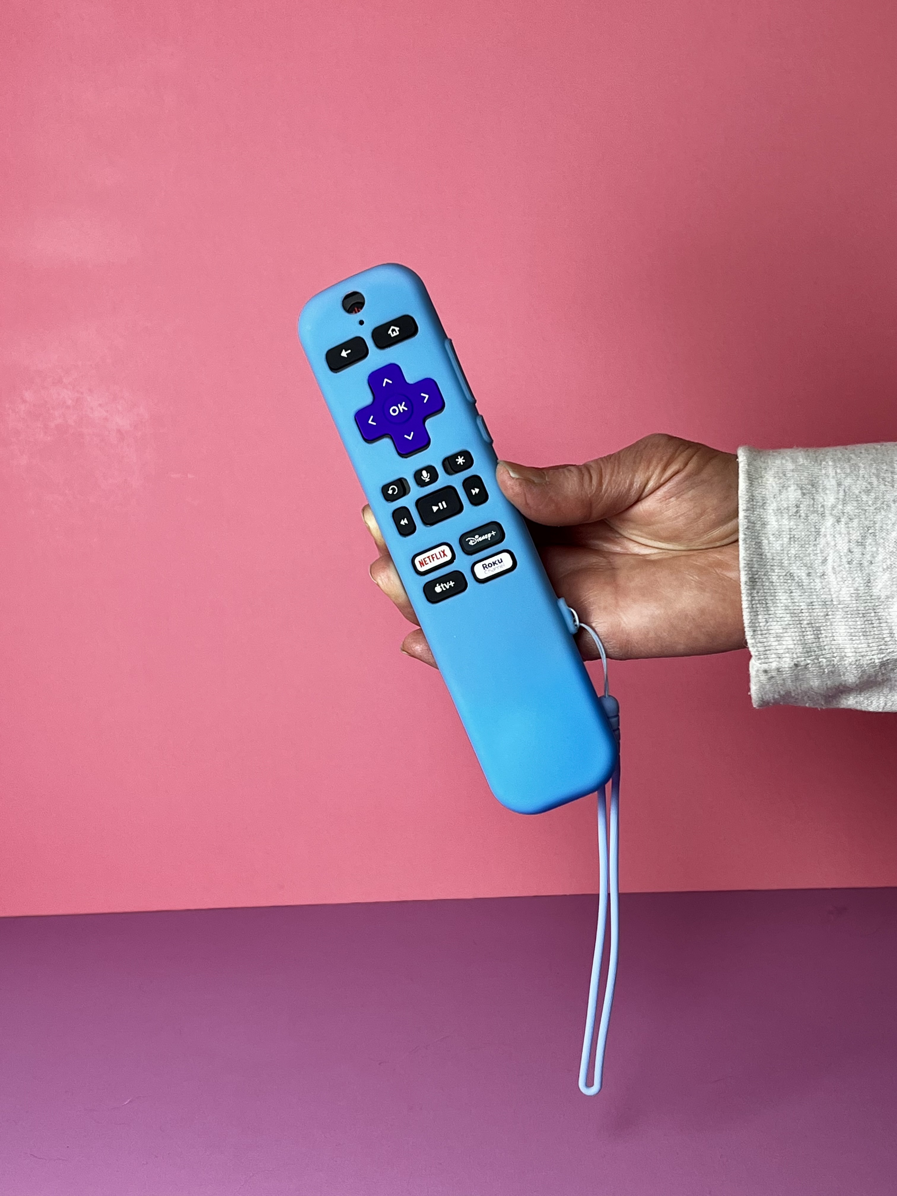 A neon blue remote case is on a Roku remote, held up by a hand. A wrist strap is dangling down. 