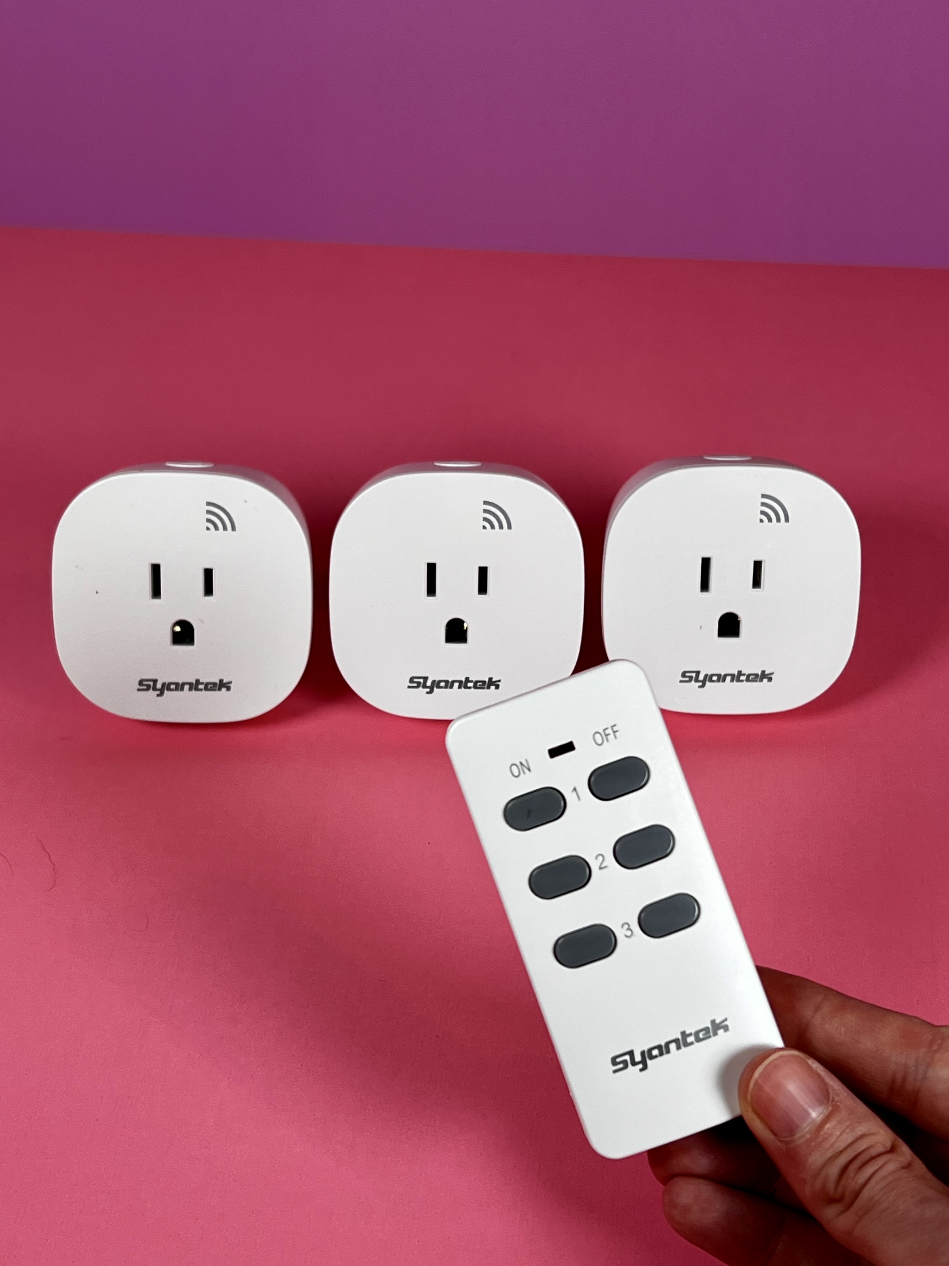 Three devices with outlet inputs are shown and a hand is holding up a single remote with on and off buttons for the three different outlets. 