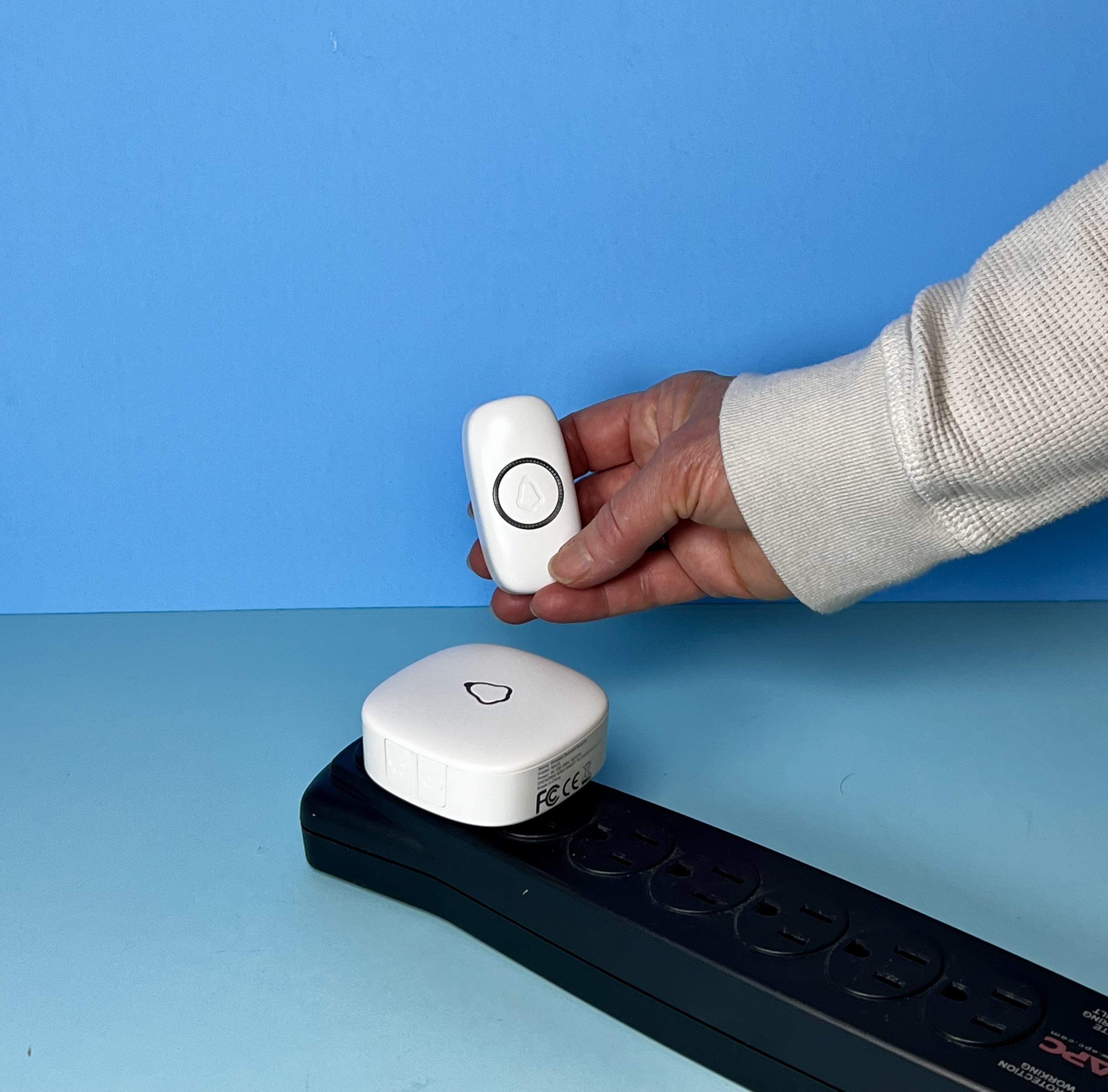 A hand is holding a remote doorbell. A device is plugged into an outlet, which makes a sound when they click it.