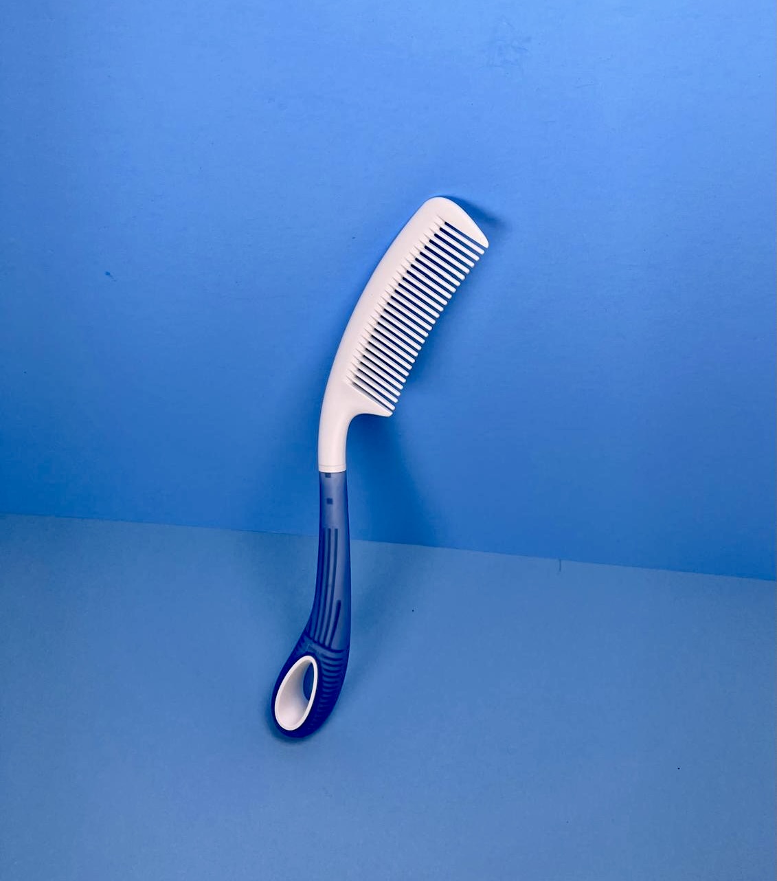 White and blue long-handled comb with an ergonomic grip against a blue background.