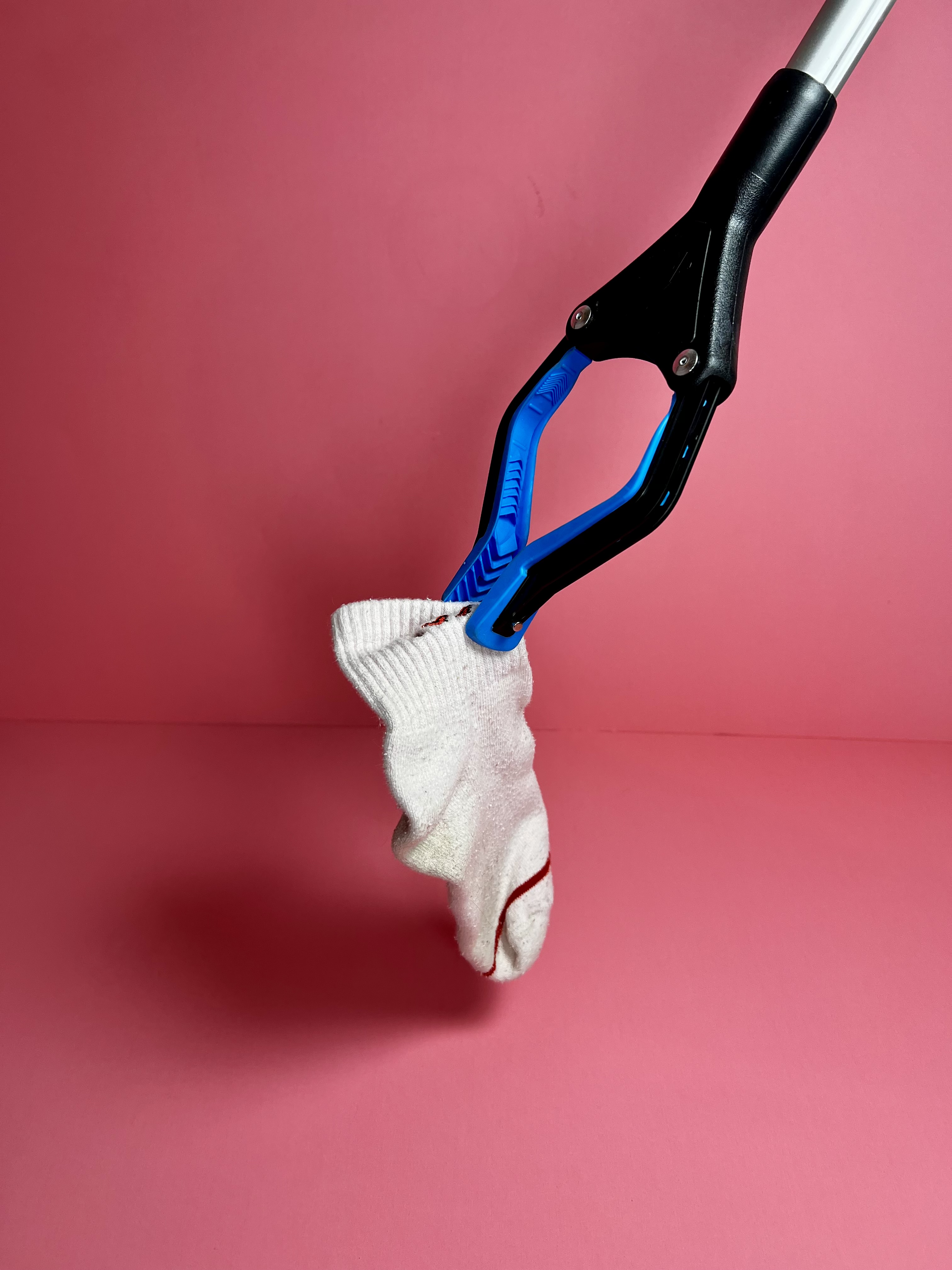 Blue and black grabber tool holding a white sock against a pink background.