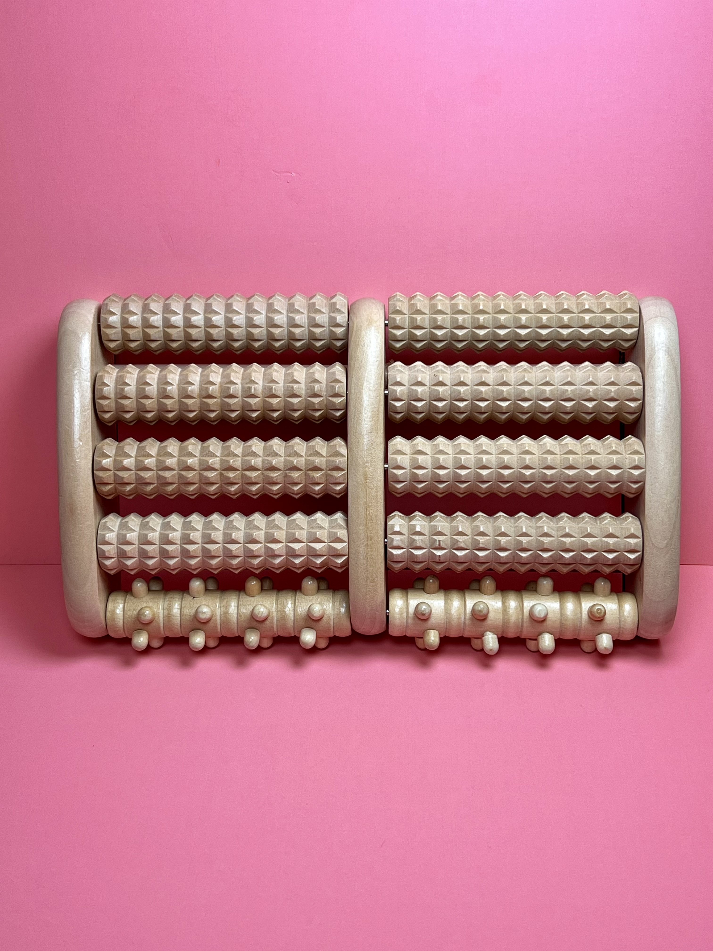 Wooden foot roller with textured and spiked rollers on a pink background.