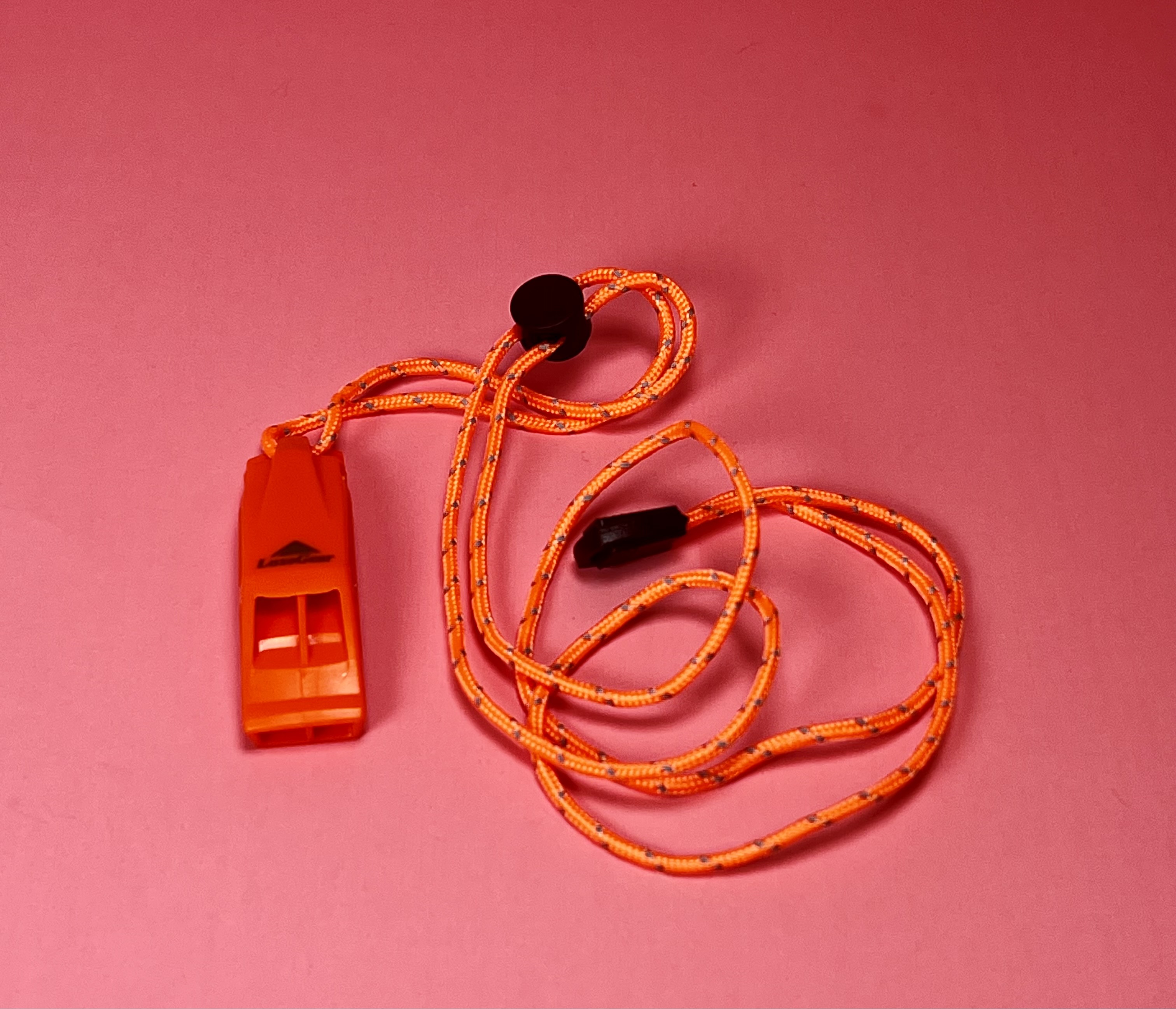 Bright orange whistle with a matching orange lanyard on a pink background.