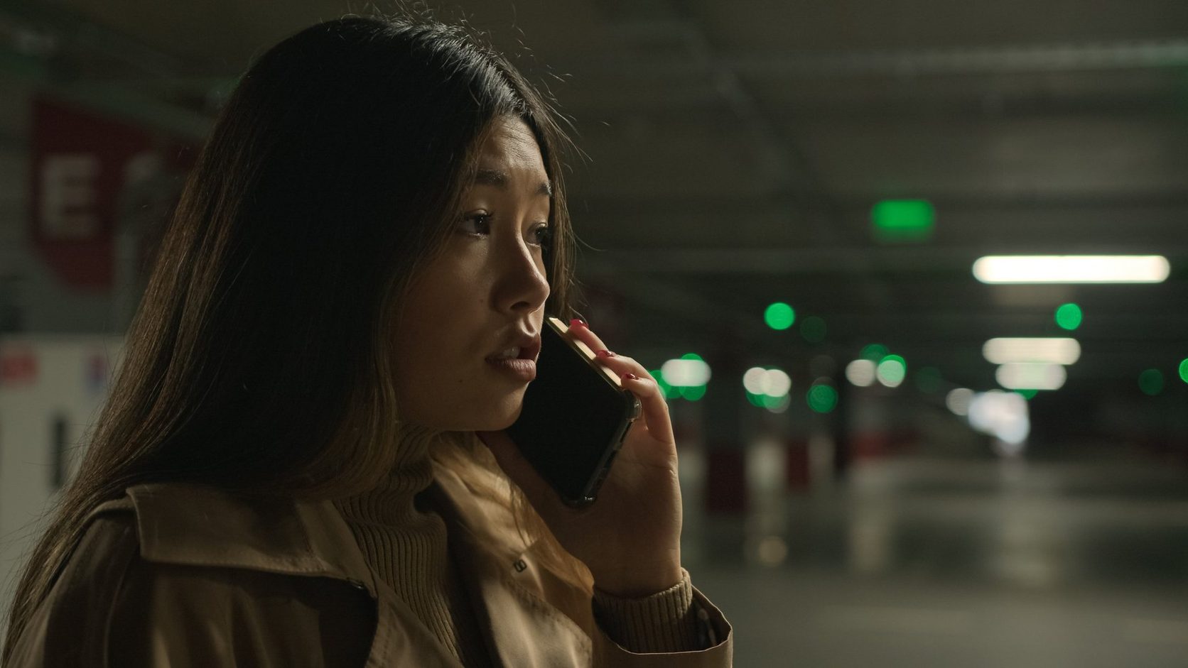 Worried woman talking on a cell phone in a dimly lit underground parking garage.