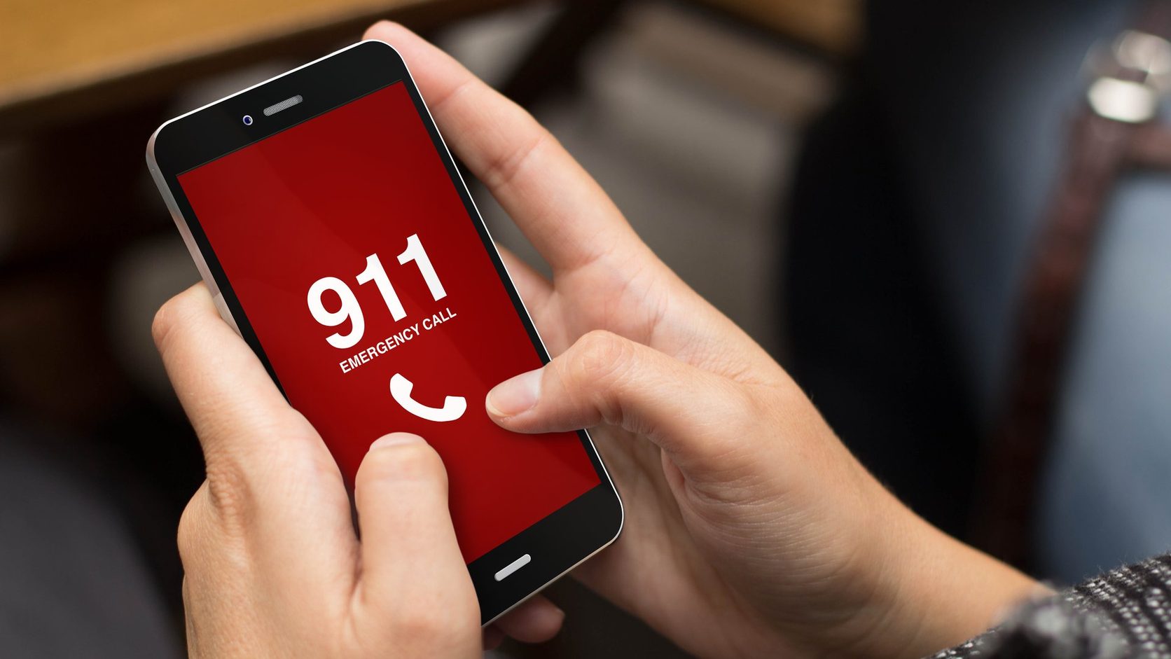 Close-up of hands holding a smartphone showing a red 911 emergency call screen.
