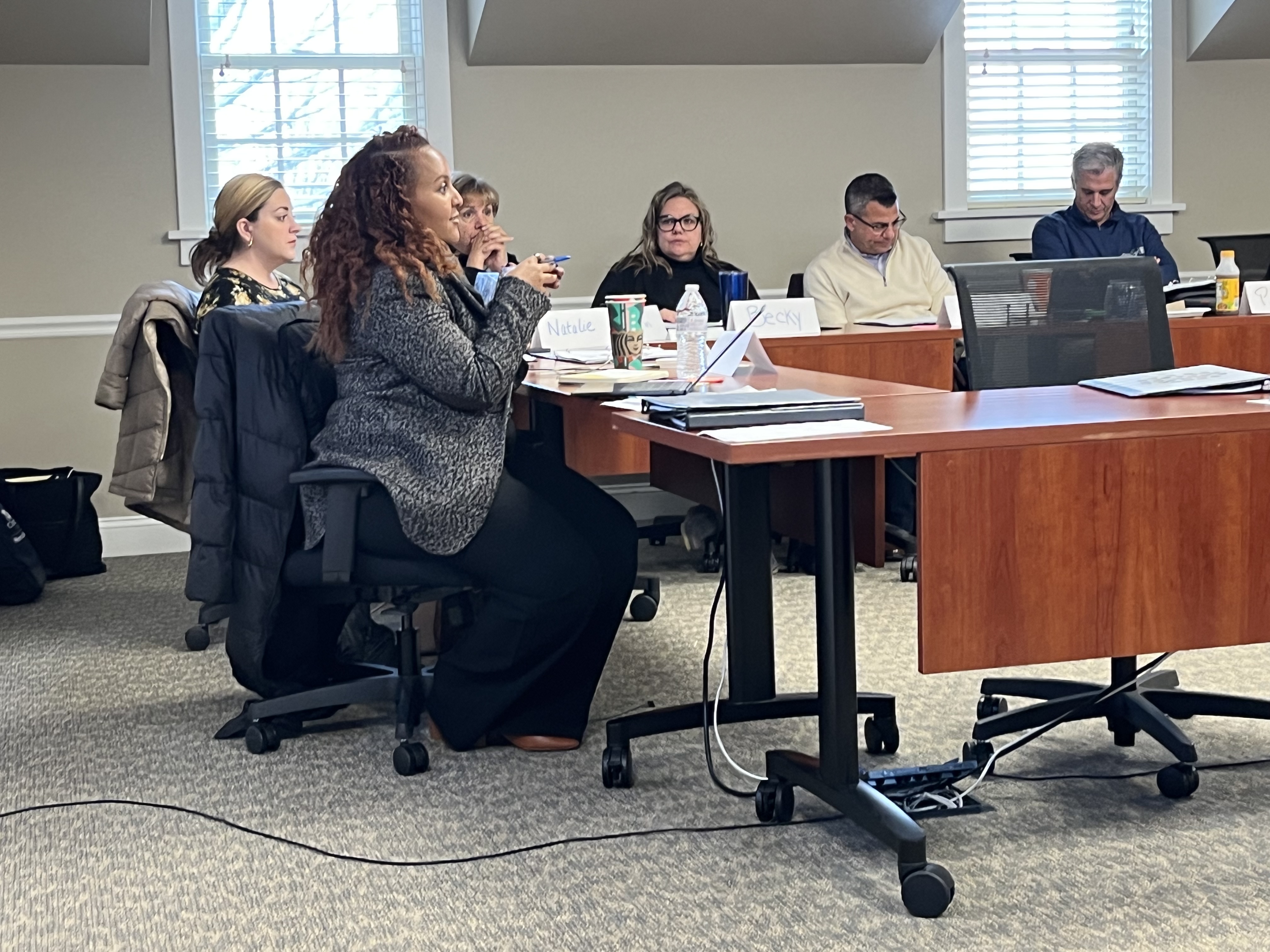Group of adults seated in a conference room, listening and taking notes during a meeting.