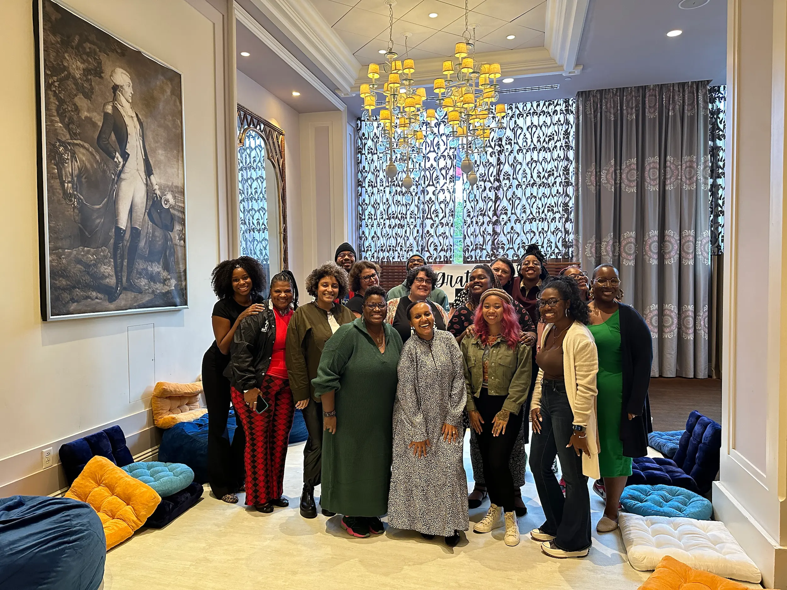 Group of smiling people posing in a decorated room with pillows, curtains, and a chandelier.