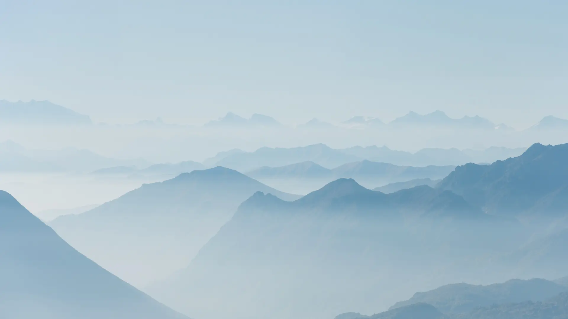 Sunset over a winding river with a vast valley and mountain range under a partly cloudy sky with the moon visible.