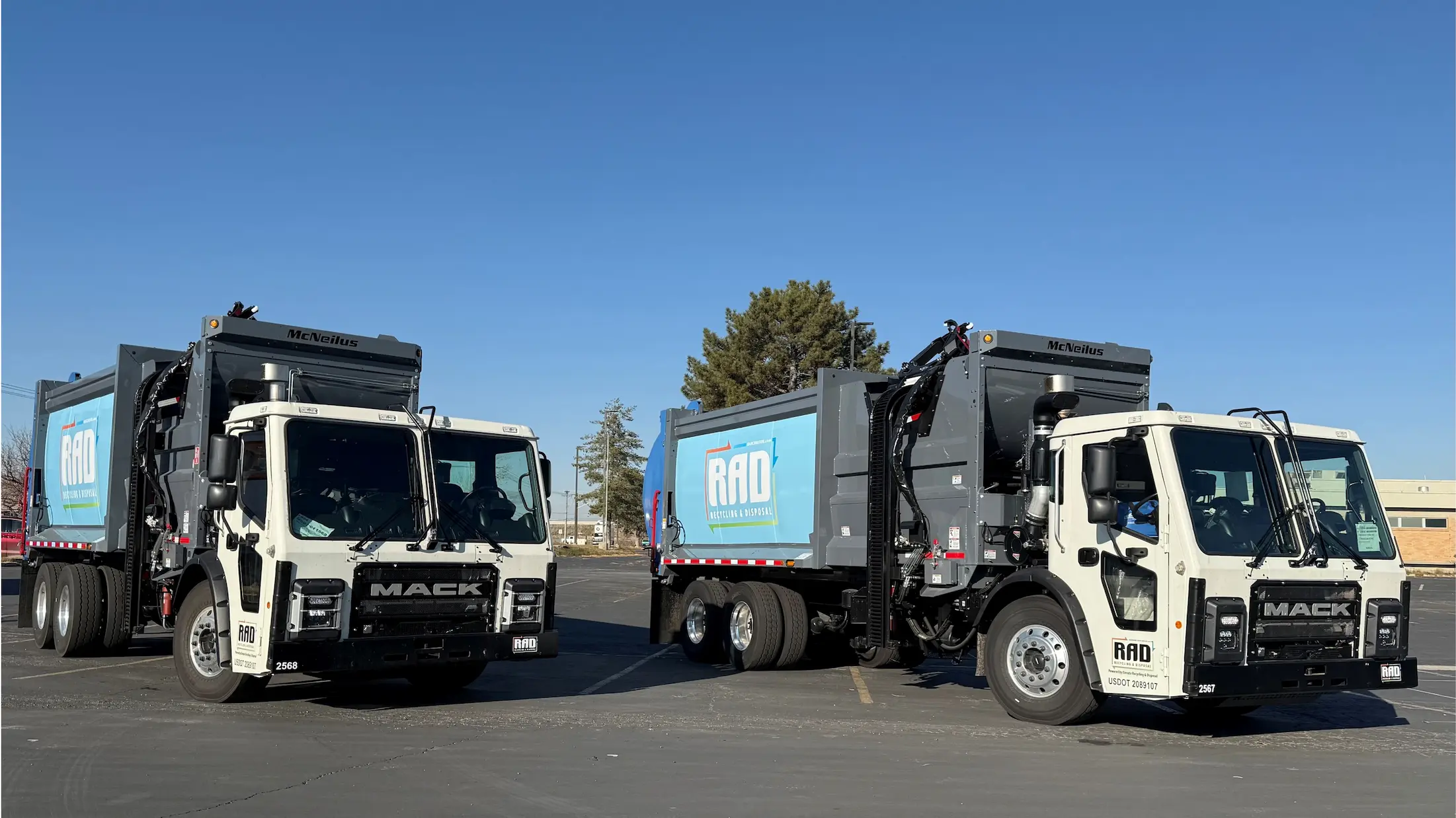 Two white Mack garbage trucks with RAD Recycling & Disposal logos parked side by side under a clear blue sky.