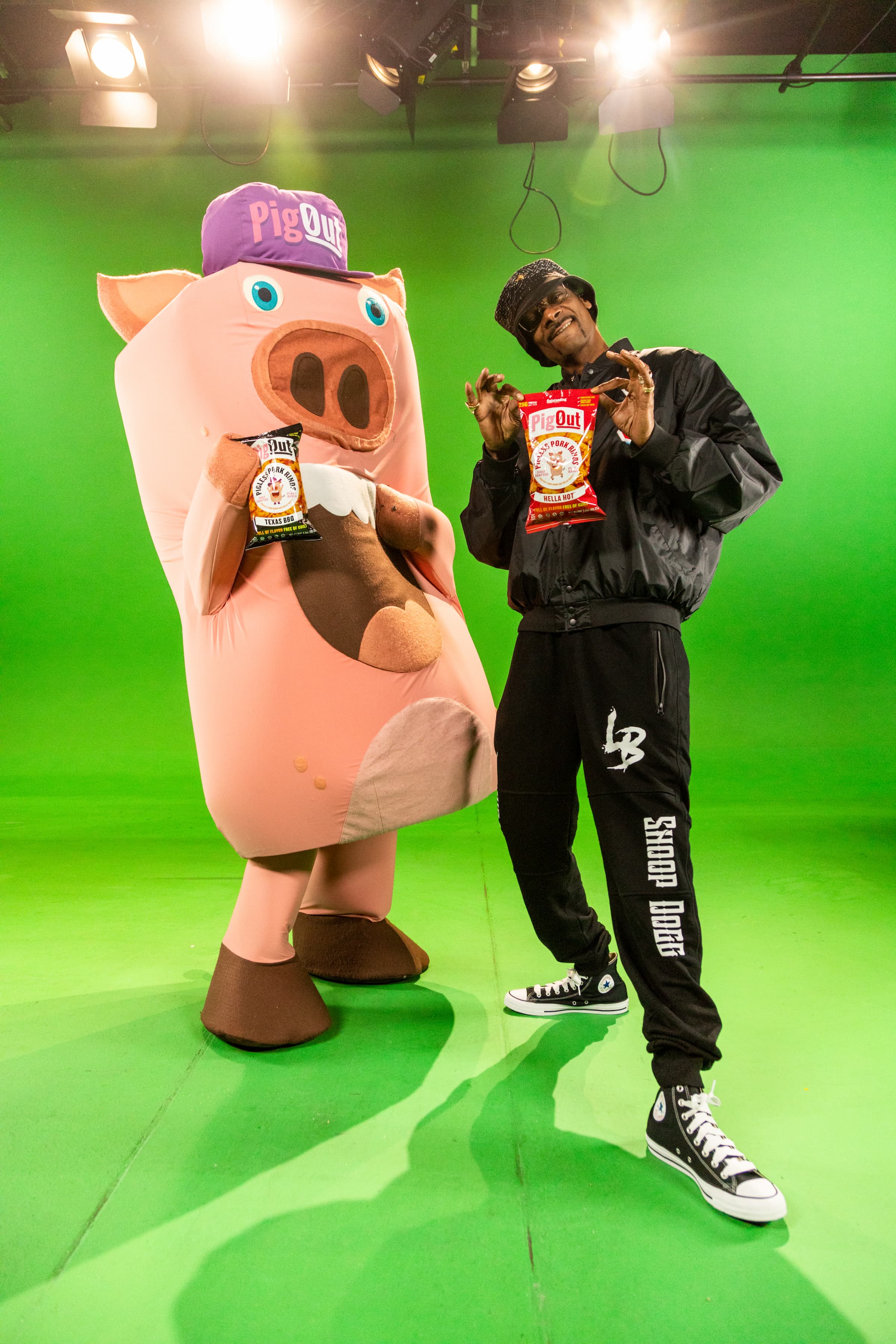 Snoop Dogg and the PigOut mascot holding snack bags on set
