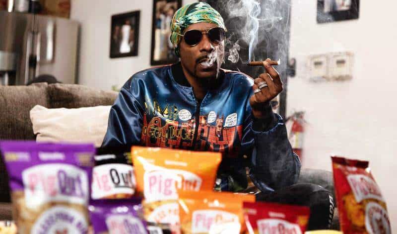 Snoop Dogg seated behind a display of PigOut snack bags