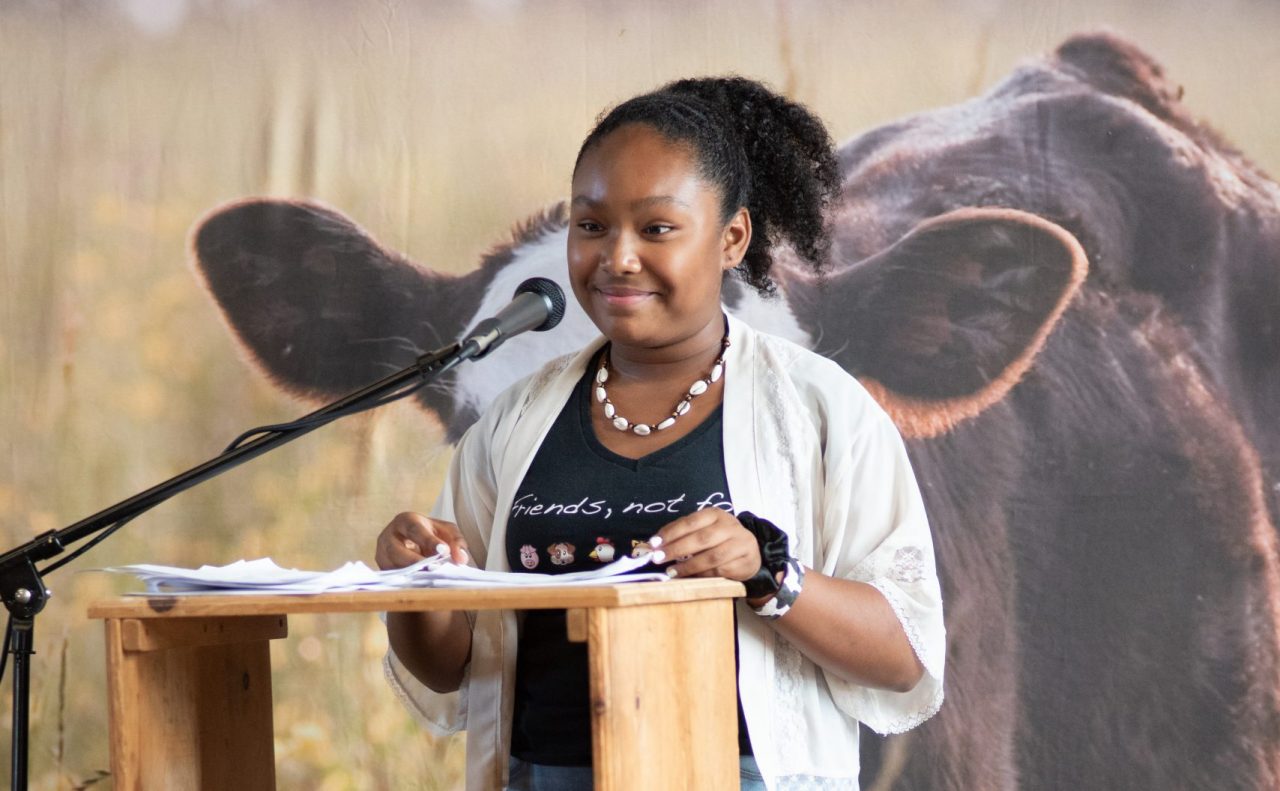 A young advocate speaking at a podium in front of a cow banner