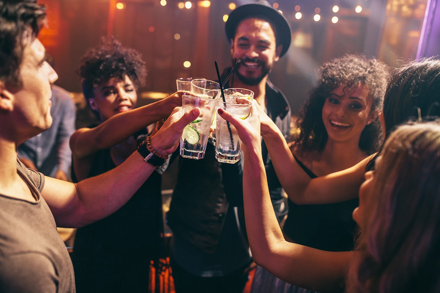 Group of friends smiling and clinking glasses with drinks at a party.