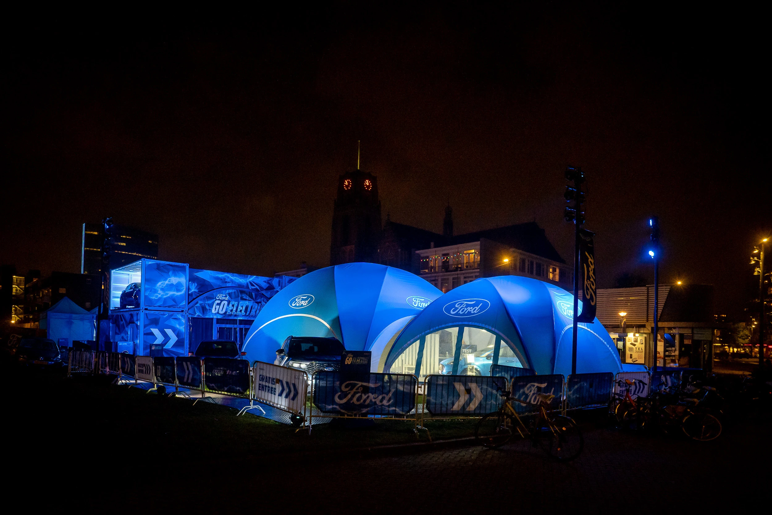 Ford electric vehicle exhibition with blue illuminated tents and cars at night in an urban setting.