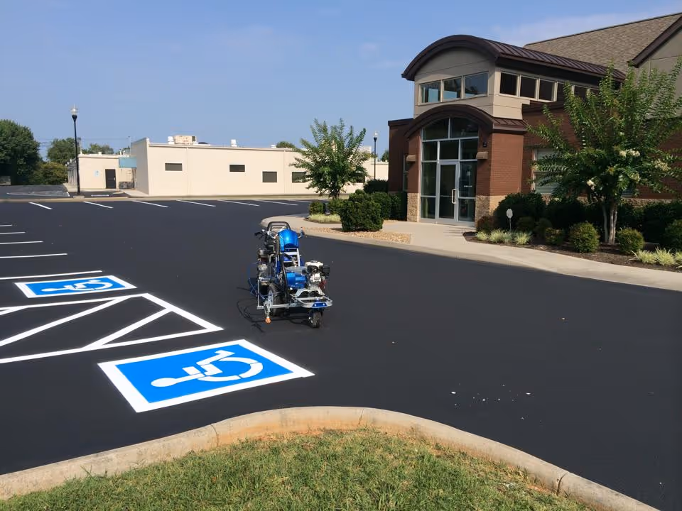 Newly painted parking lot with bright blue handicap parking symbols and a line marking machine in front of a brick and stone building.