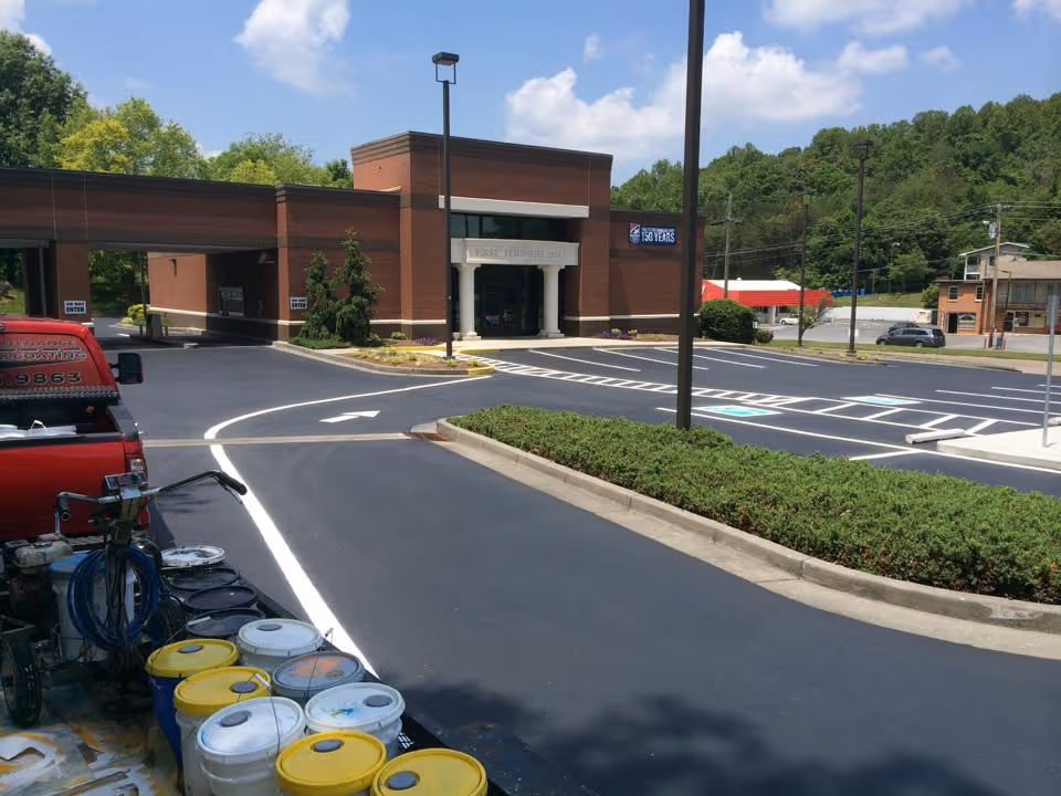 Freshly paved and painted parking lot at a brick building with a sign reading First Tennessee Bank under a partly cloudy sky.