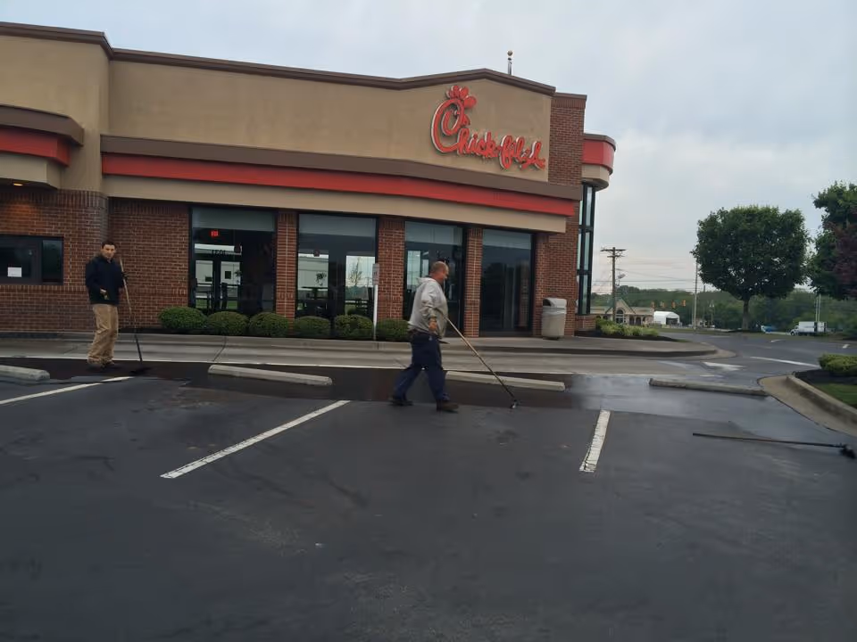Two men cleaning the parking lot in front of a Chick-fil-A restaurant on an overcast day.