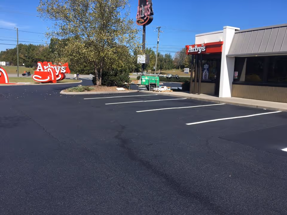 Empty parking lot of an Arby's restaurant with clear blue sky and trees in the background.