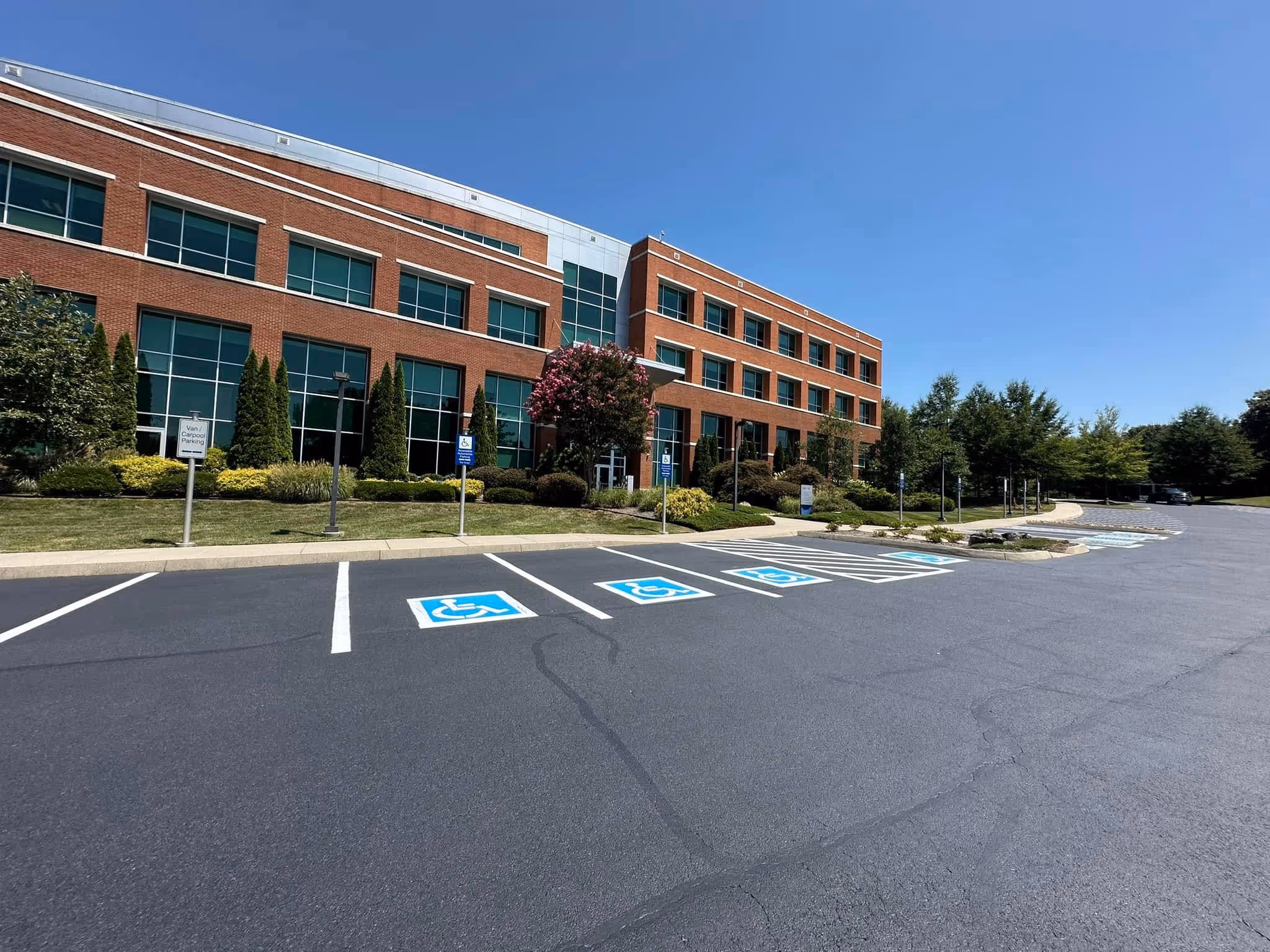 Three-story brick office building with large windows and multiple handicapped parking spaces in front under a clear blue sky.
