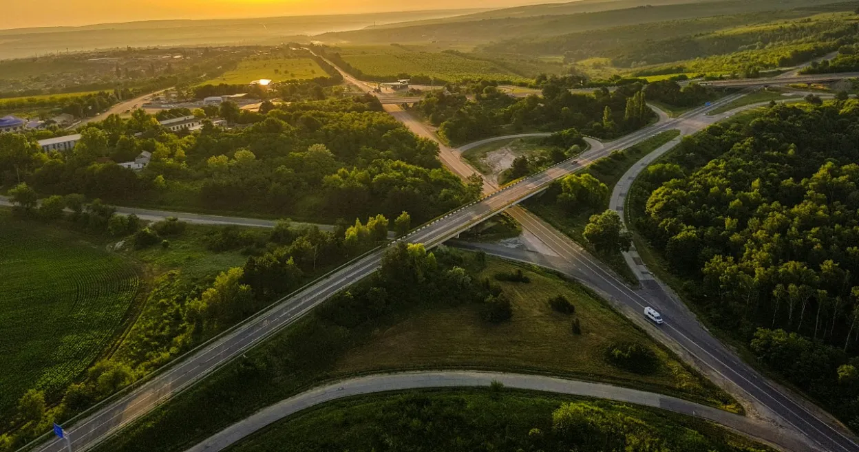 Aerial view of highway interchange surrounded by green fields and trees at sunset.