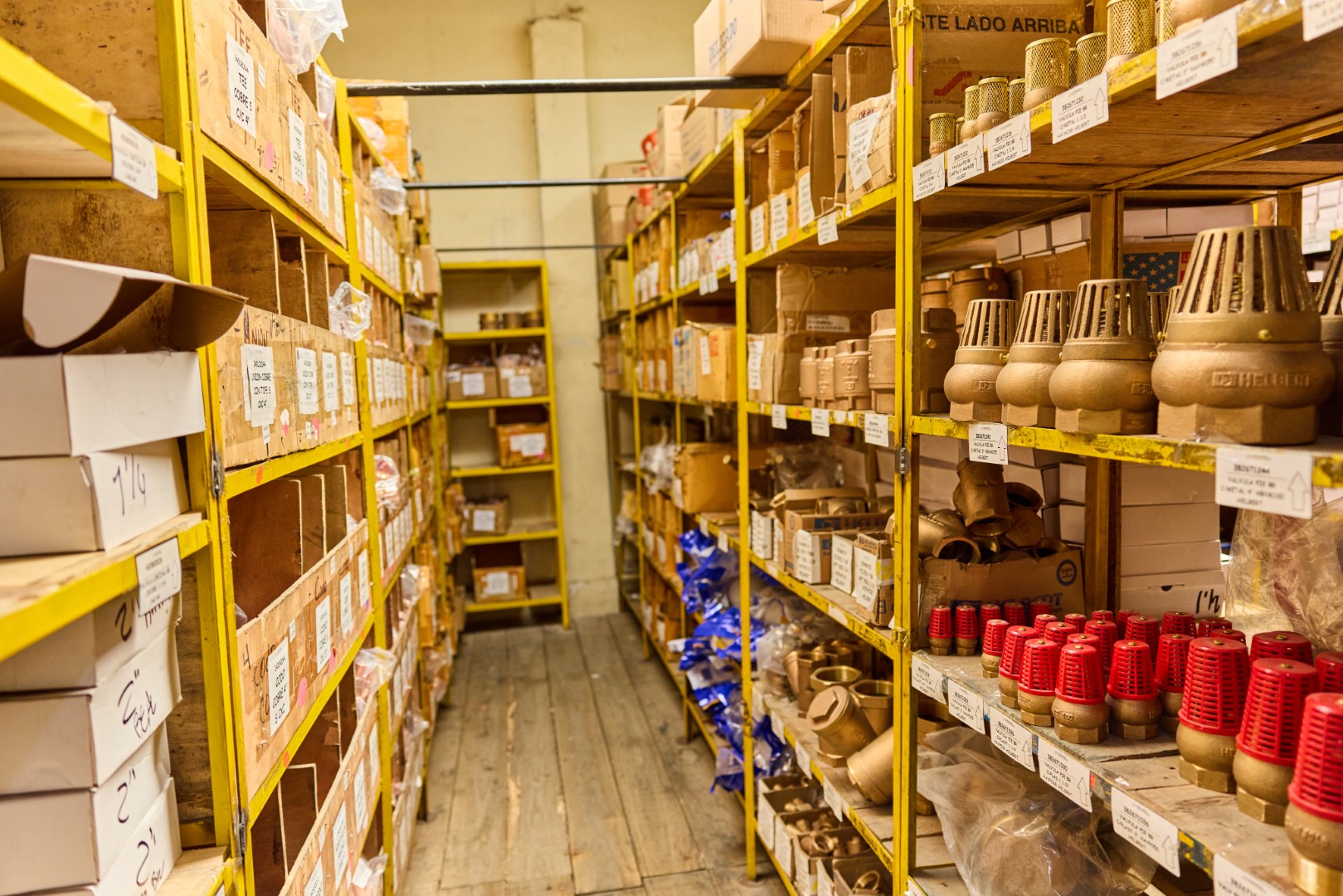 Shelves with organized plumbing parts and fittings in a storage room with wooden floor.