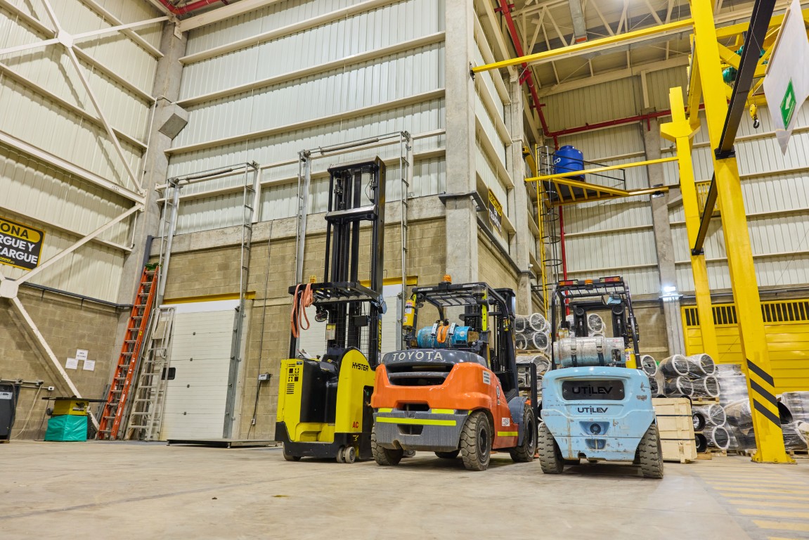 Three forklifts parked inside a large warehouse with metal walls and stacked goods.