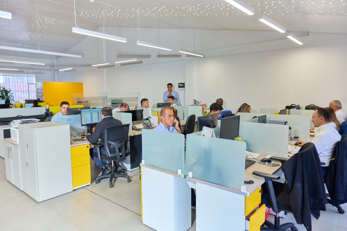Modern office with multiple workers at desks separated by frosted glass dividers and yellow drawers.
